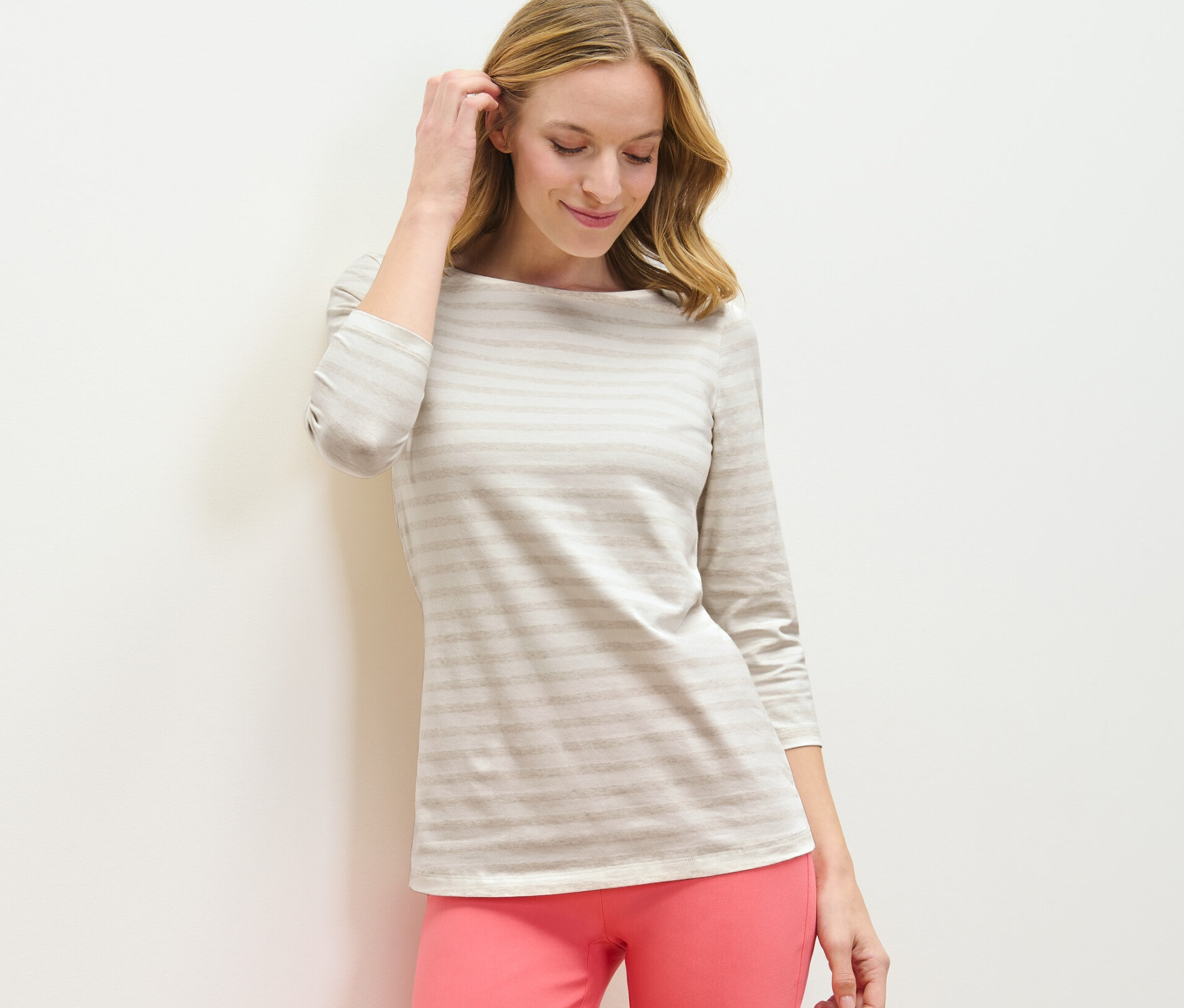 Frau berührt ihr Haar und trägt ein gestreiftes Shirt mit 3/4-Arm und eine pinke Hose.