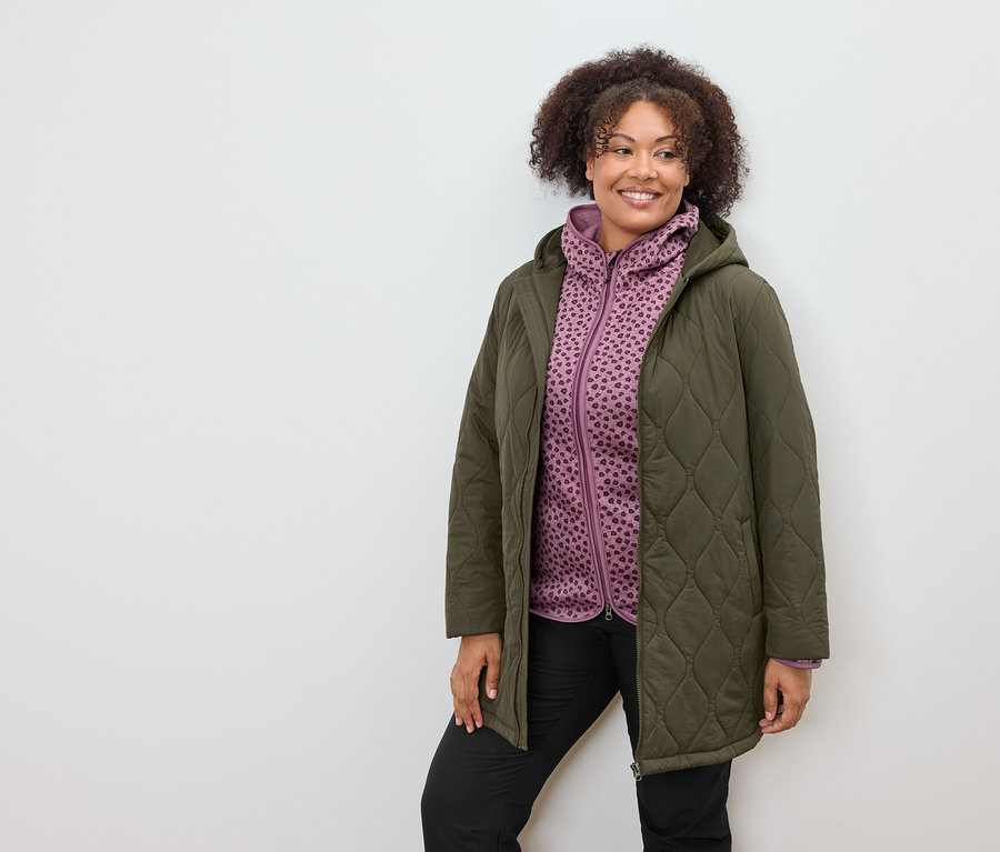 Frau trägt einen olivgrünen Steppmantel und einen lila gemusterten Kapuzenpullover.