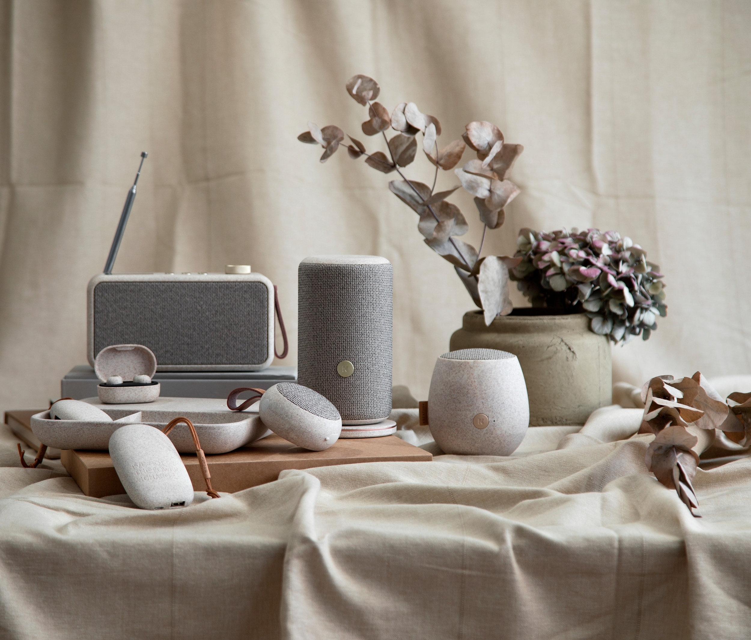 Verschiedene Kreafunk Care Lautsprecher und aBEAN Kopfhörer sind auf einem Stoffhintergrund angeordnet.