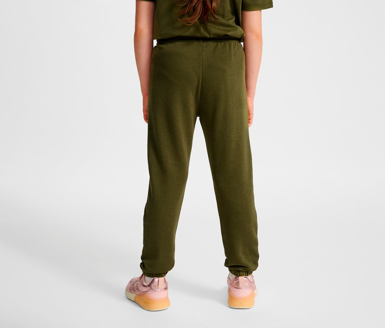 Rückansicht eines Kindes, das grüne HUMMEL HMLJR Base Regular Pants und rosa Schuhe trägt.