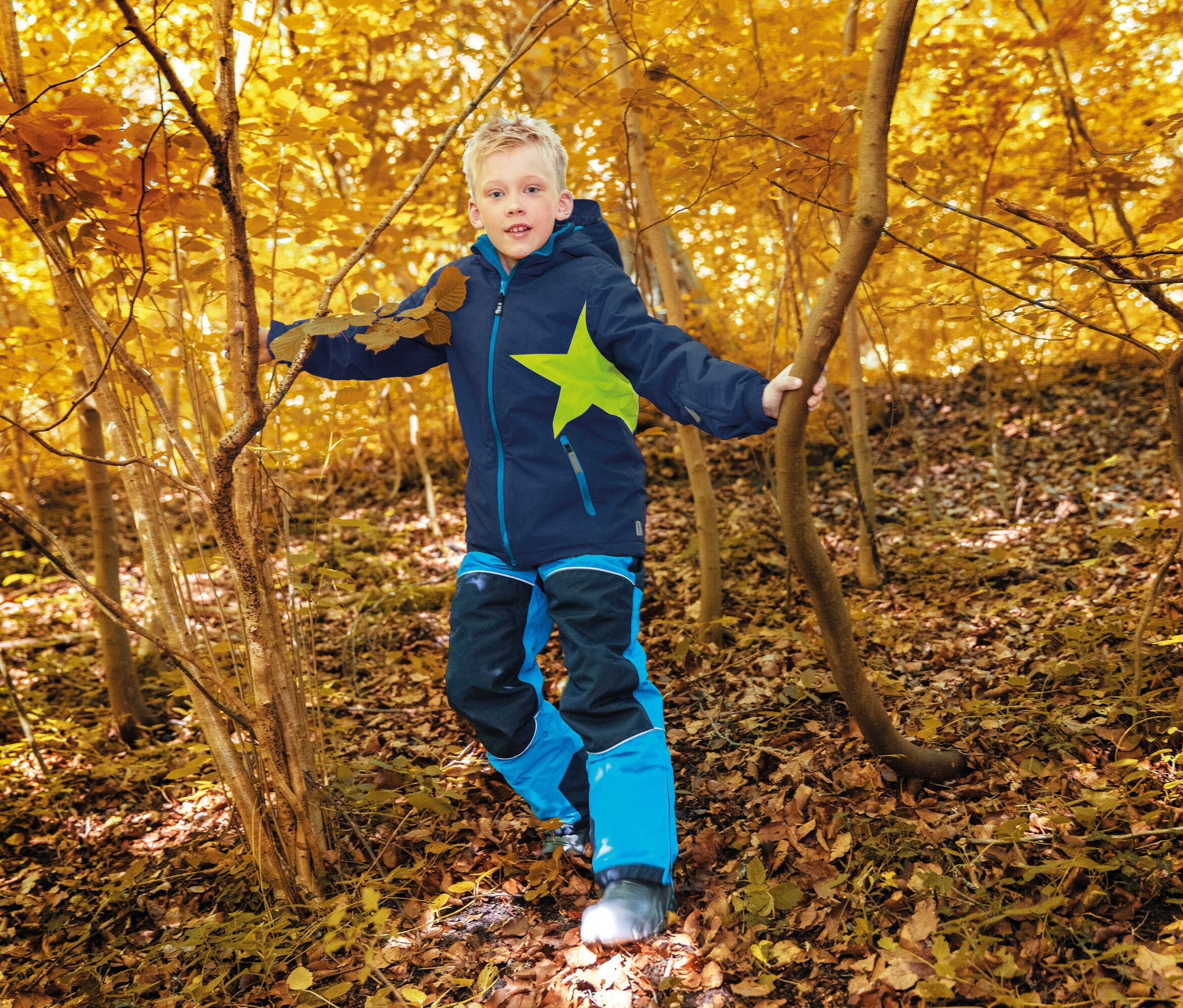Ein Junge in blau-schwarzer Kleidung mit einem Stern geht durch einen Herbstwald.
