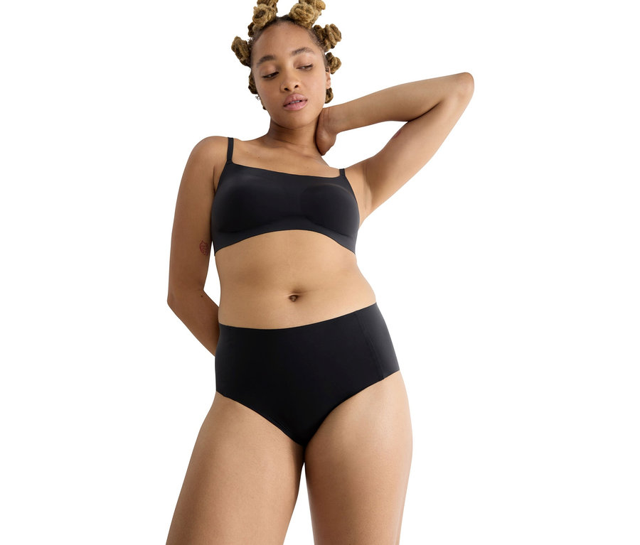 Frau mit Dutt trägt schwarzen BH und hochgeschnittene Unterhose.