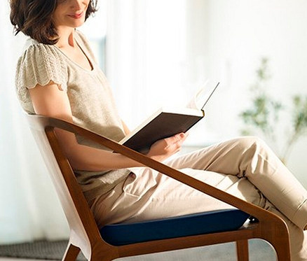 Frau sitzt auf einem Holzstuhl mit blauem TEMPUR® Sitzkissen und liest ein Buch.