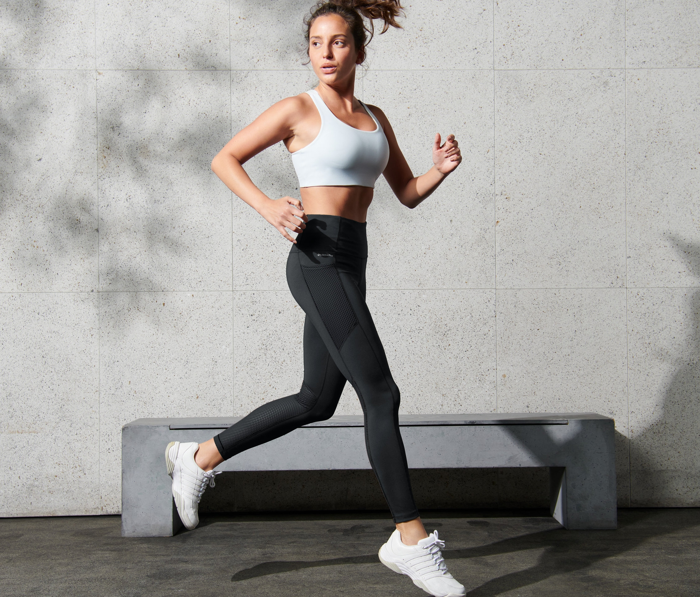 Frau mit weißem Sport-BH und Sporttight mit Mesh beim Laufen.