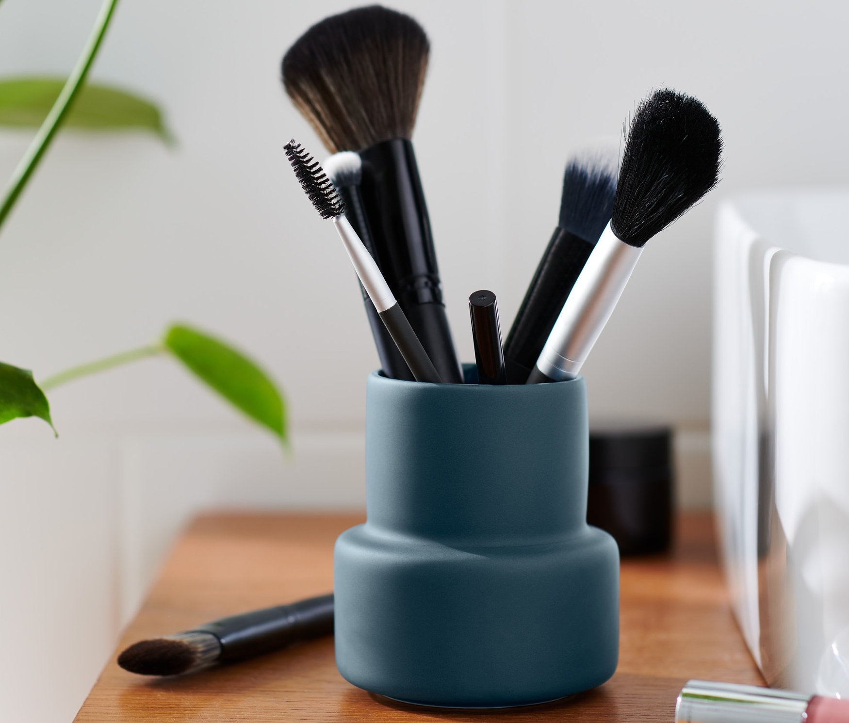 Blaues Utensilo mit Make-up-Pinsel auf einem Holzschrank.