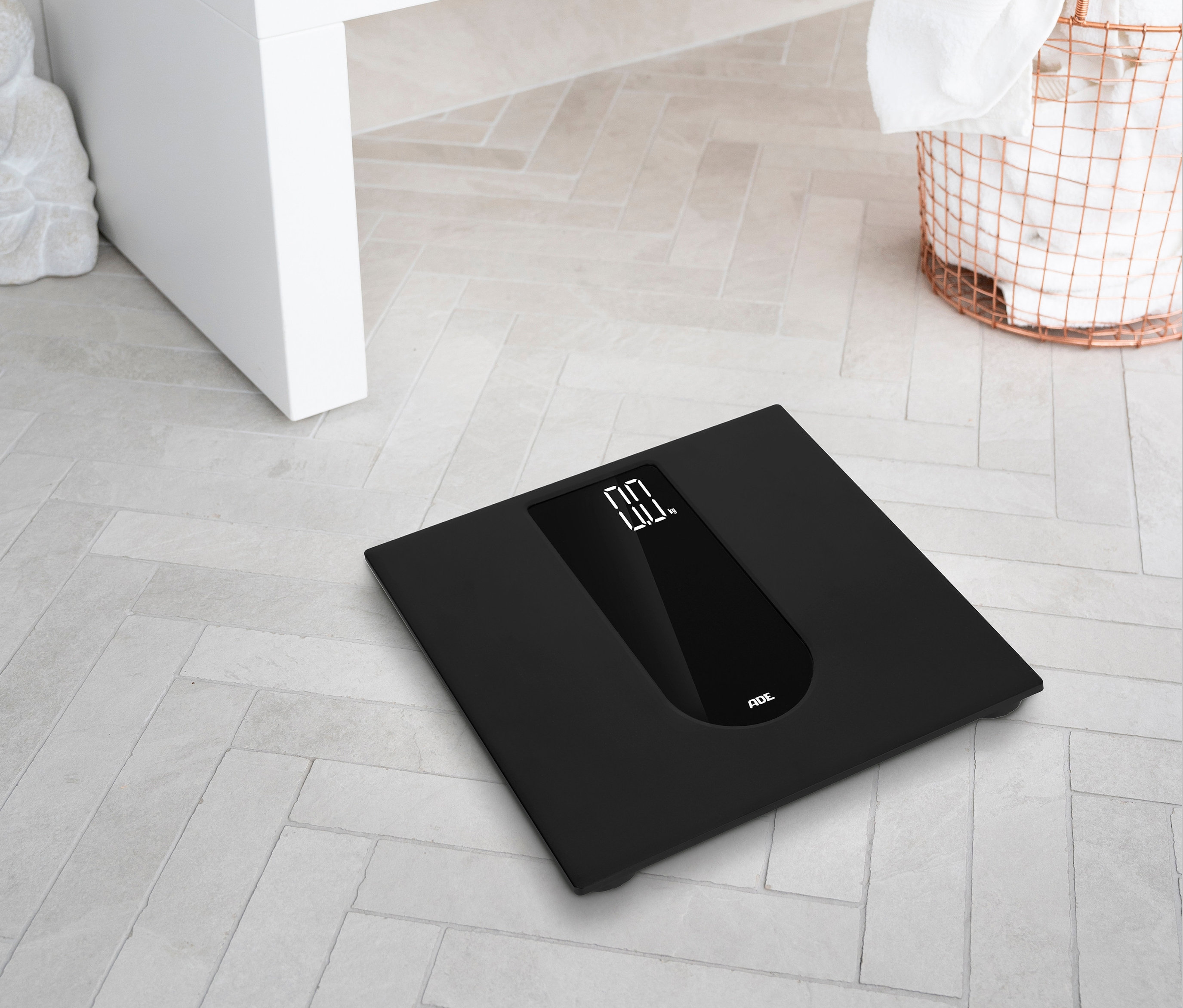 Eine schwarze digitale ADE Personenwaage liegt auf einem Badezimmerboden.