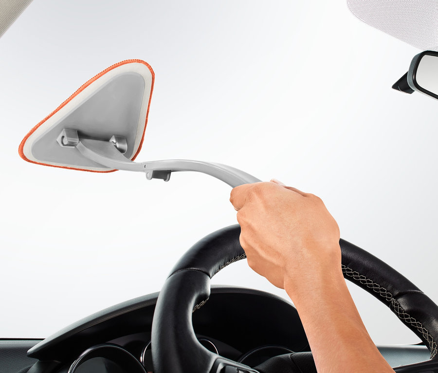 Eine Hand hält einen Autoscheibenreiniger und reinigt die Windschutzscheibe eines Autos.