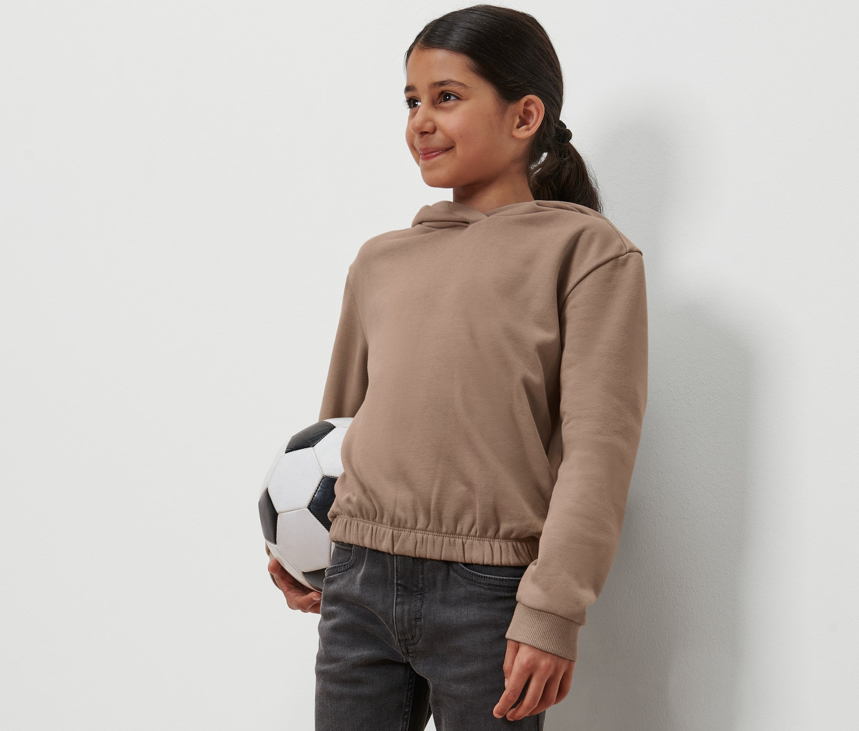 Mädchen hält einen Fußball und trägt einen Kinder-Hoodie.