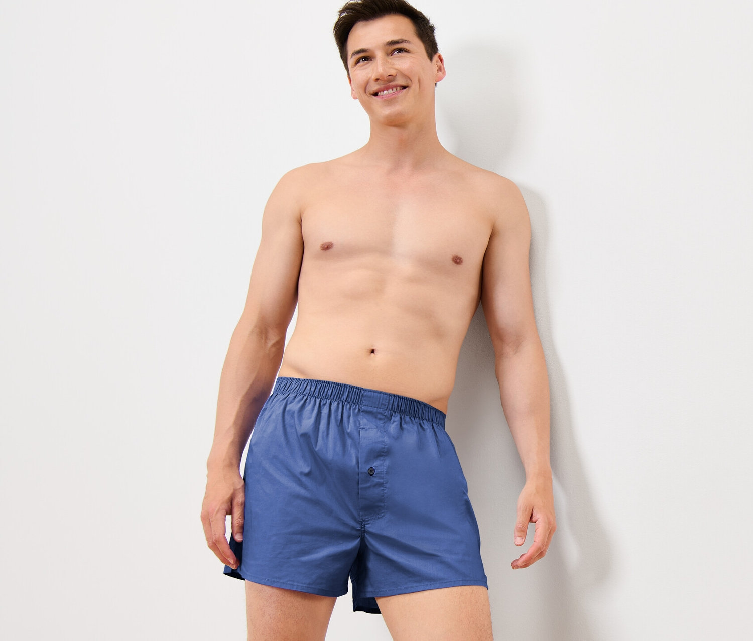 Mann, an eine Wand gelehnt, trägt blaue 4 Web-Boxershorts.