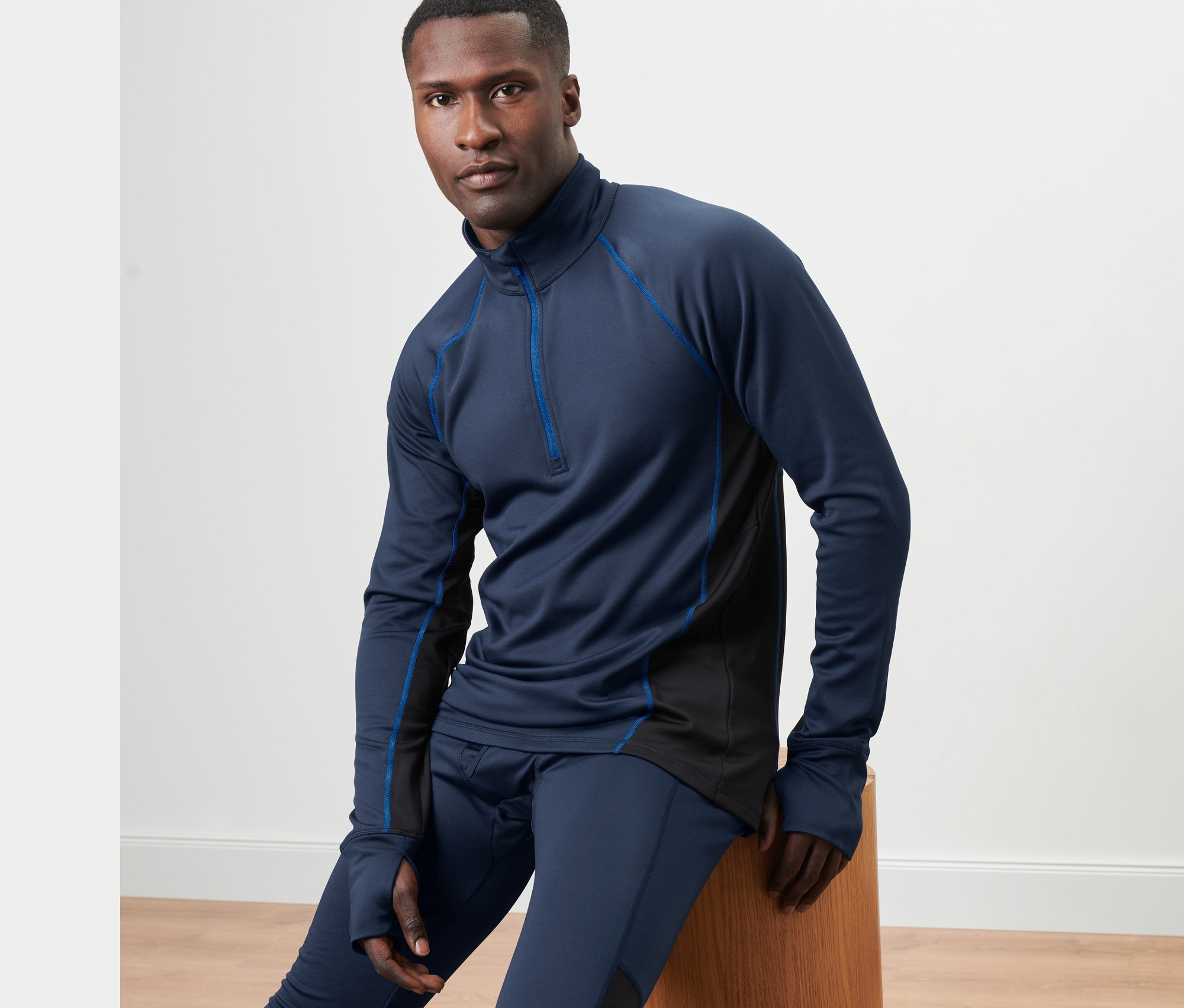 Mann sitzt auf einem Holzhocker und trägt ein blaues Thermo-Funktionsshirt.