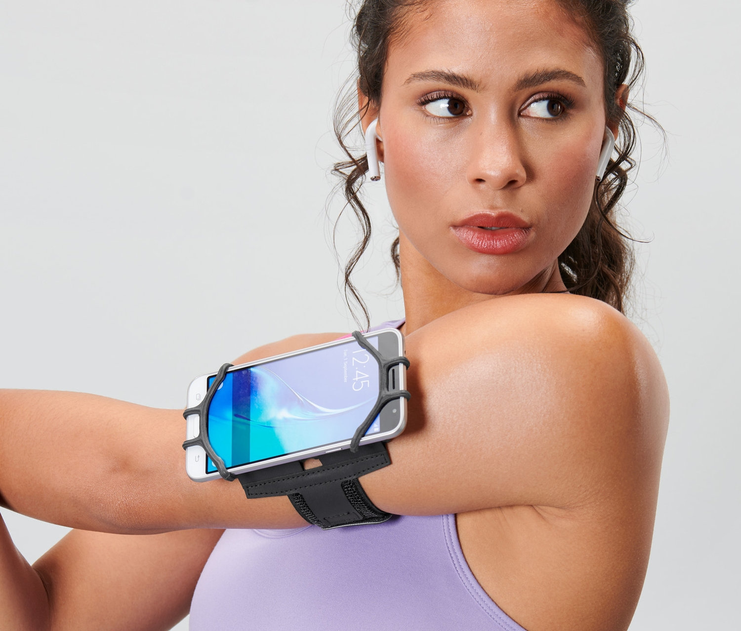 Frau dehnt Arm mit Smartphone-Sportarmband am Oberarm.