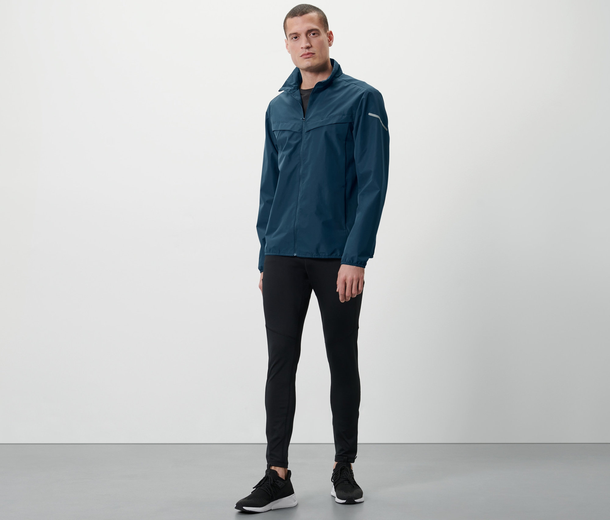 Mann steht und trägt eine blaue Windprotection-Jacke.