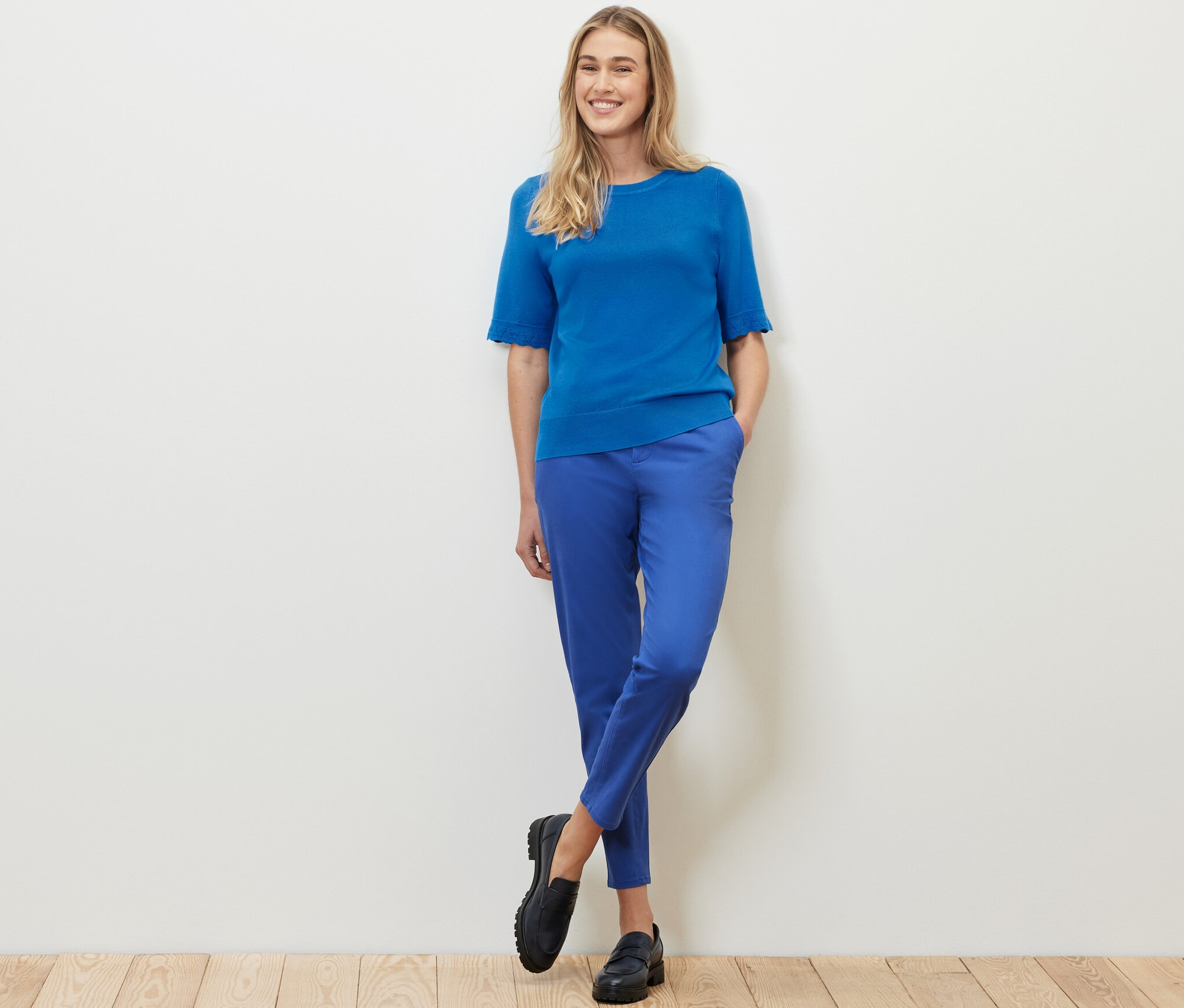 Frau posiert in kobaltblauem Feinstrickpullover und blauer Hose.