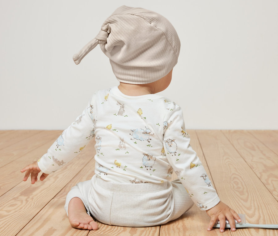 Baby sitzt mit dem Rücken zur Kamera und trägt 2 Baby-Jerseymützen.