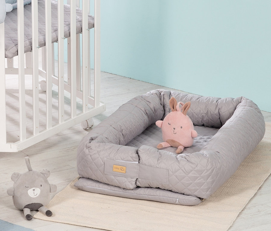 Graue Roba 3-in-1 Babylounge mit Plüschhase auf beigem Teppich neben einem weißen Kinderbett.