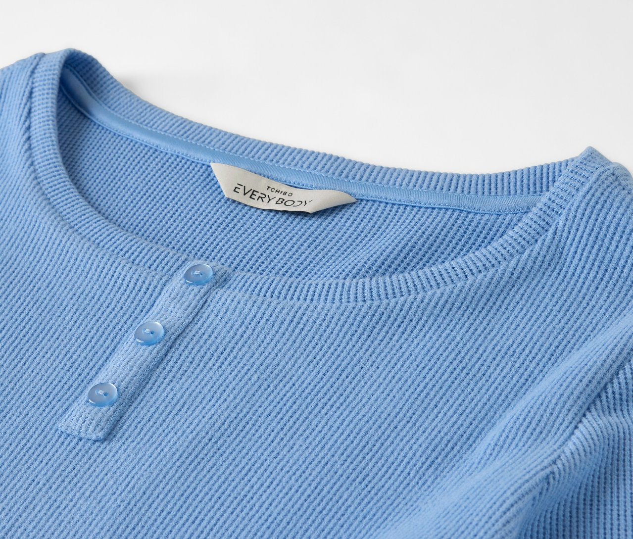 Detailaufnahme eines hellblauen, langärmligen Oberteils mit drei Knöpfen.