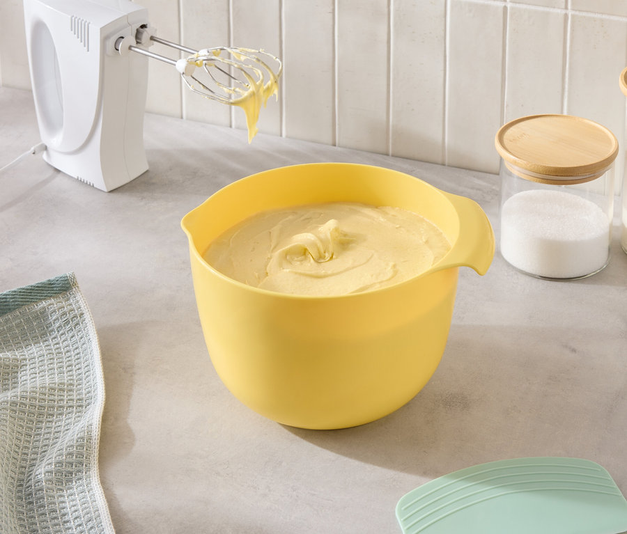 Auf der Küchentheke stehen eine gelbe Schüssel mit Teig, ein Mixer und Gläser mit Zucker und Mehl.