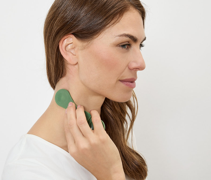 Frau massiert ihren Nacken mit einem grünen Massagegerät.