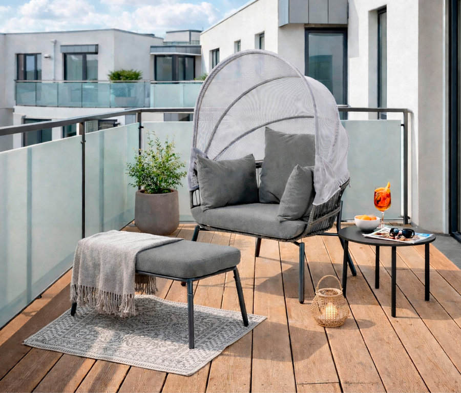 Auf einer Terrasse steht ein Leco Sessel mit Fußhocker, ein Getränk und eine Pflanze auf einem Tisch.