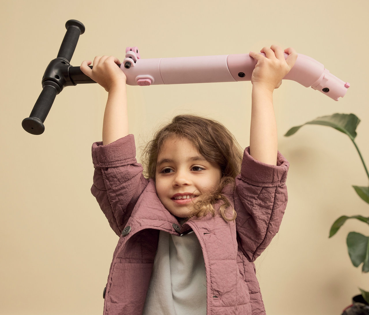 Mädchen hält PUKY Roller PUSH über dem Kopf. Der Roller ist rosa und hat schwarze Griffe.