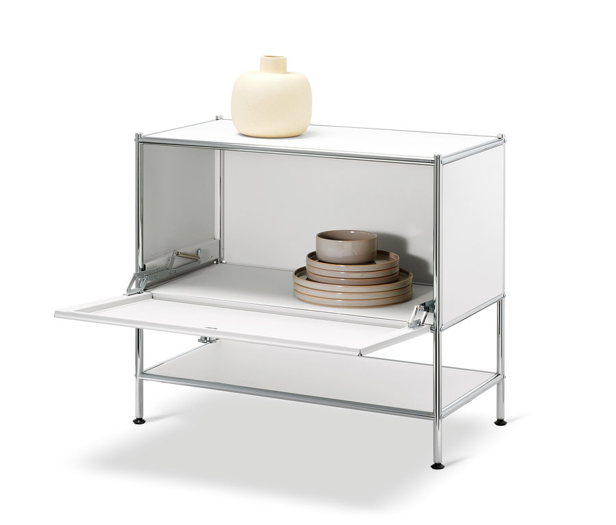 Weißes Sideboard »CN3« mit geöffneter Klappe. Auf der Oberseite befindet sich eine beige Vase, im Inneren des Schranks befindet sich ein Satz Teller und Schalen.