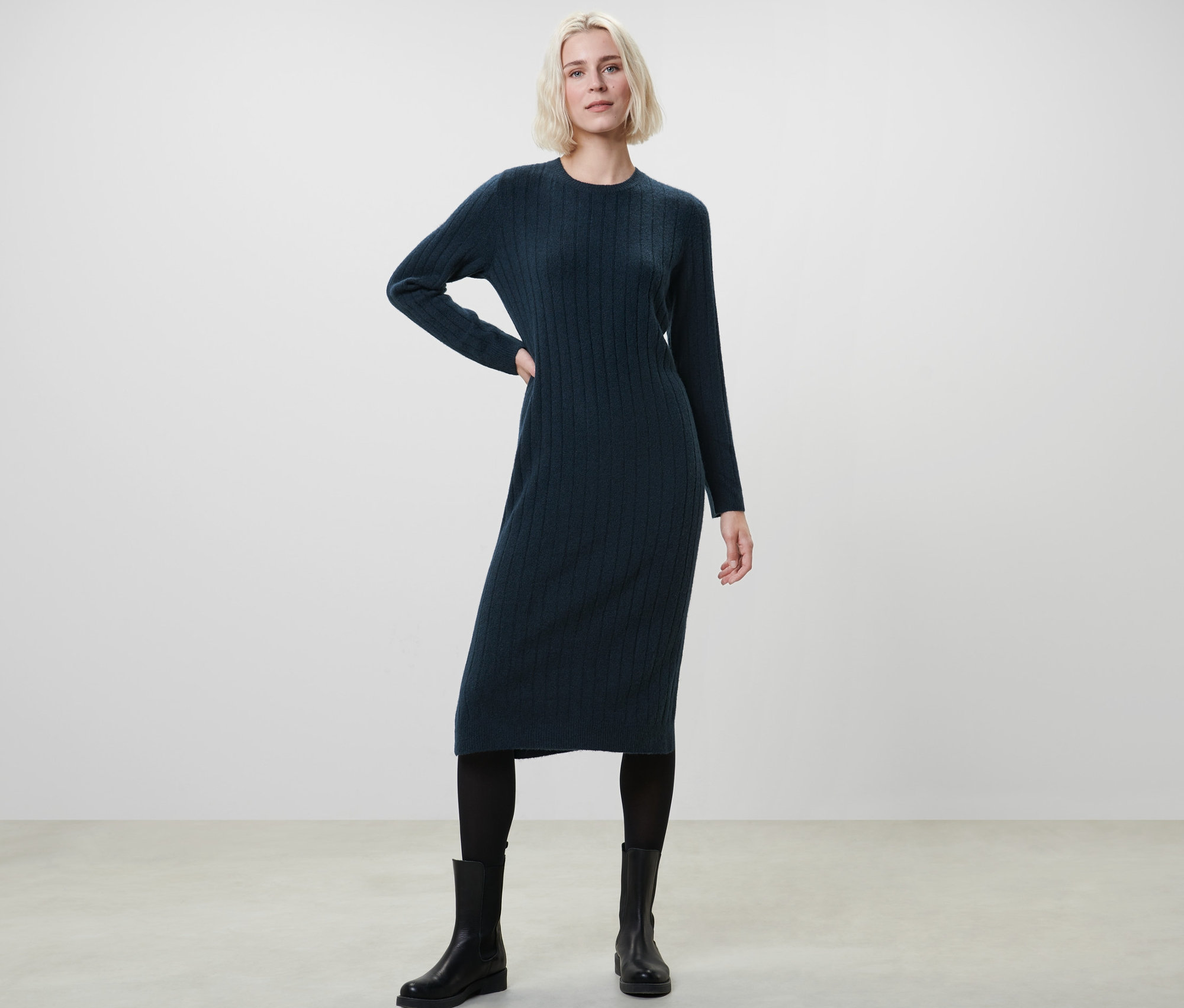 Frau posiert in geripptem, dunkelblauem Strickkleid.