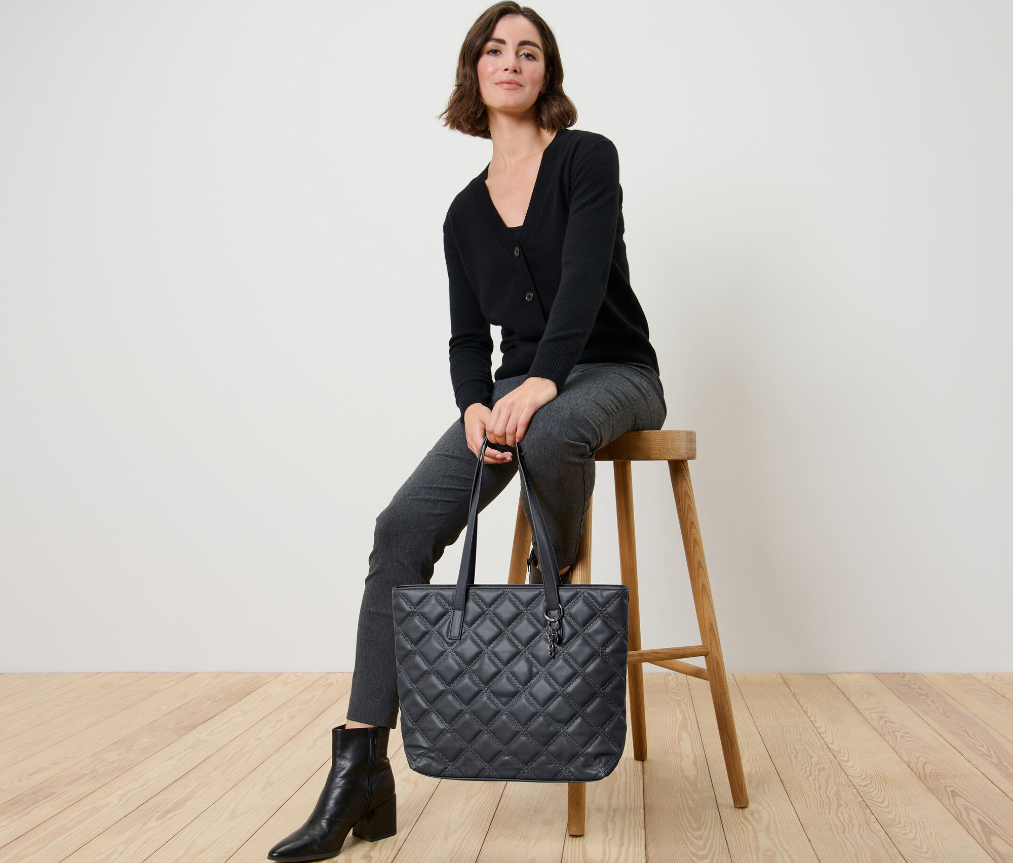 Frau sitzt auf einem Hocker und hält einen Shopper.