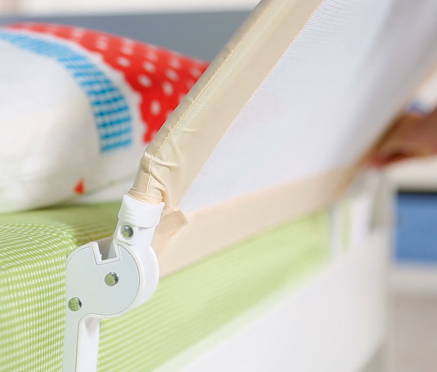Detail eines beigen roba Bettschutzgitters »Klipp-Klapp«, das an einer Matratze mit einem bunten Kissen befestigt ist.