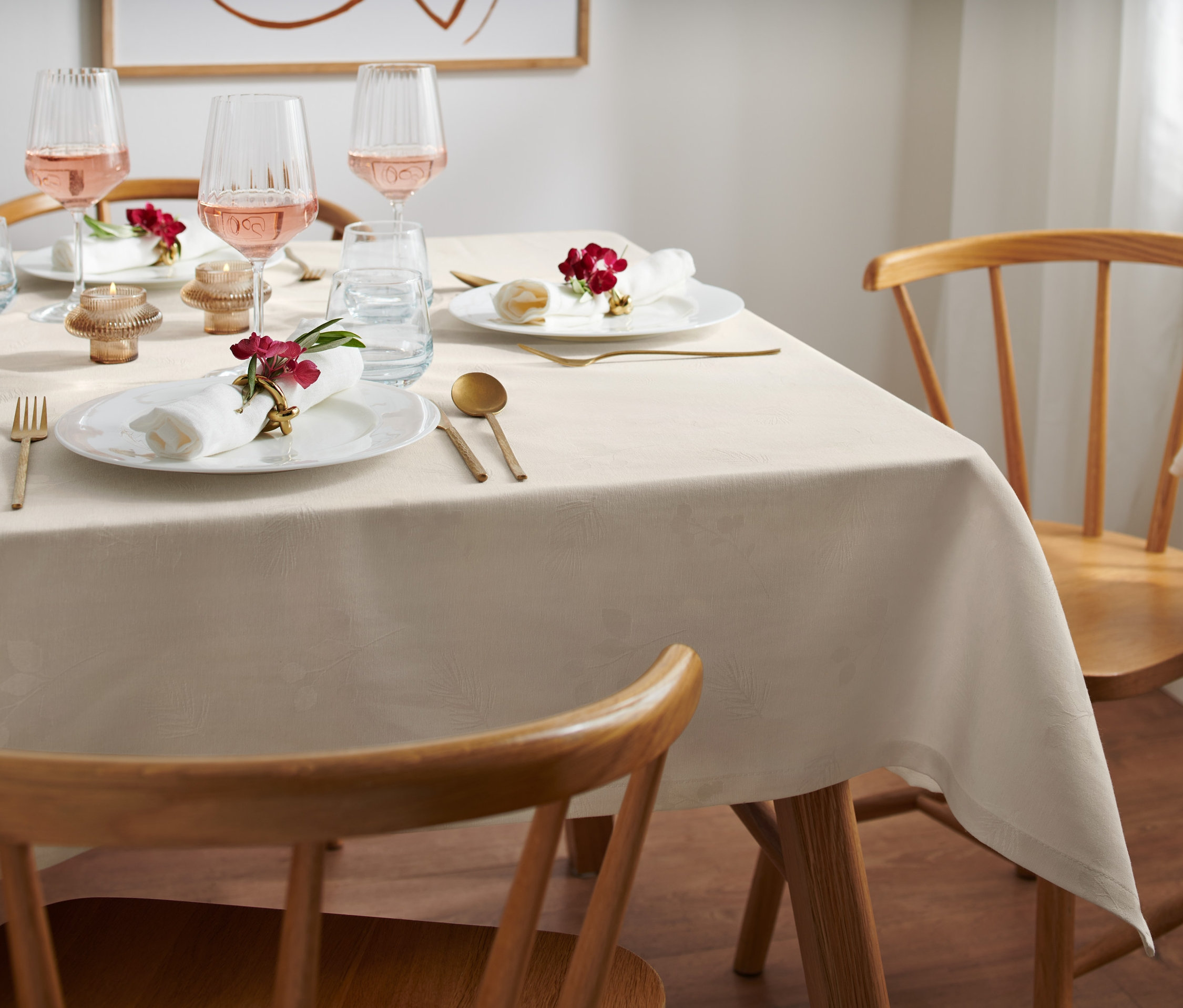 Gedeckter Tisch mit einer cremefarbenen Jacquard-Tischdecke, Tellern, Gläsern und Blumen.