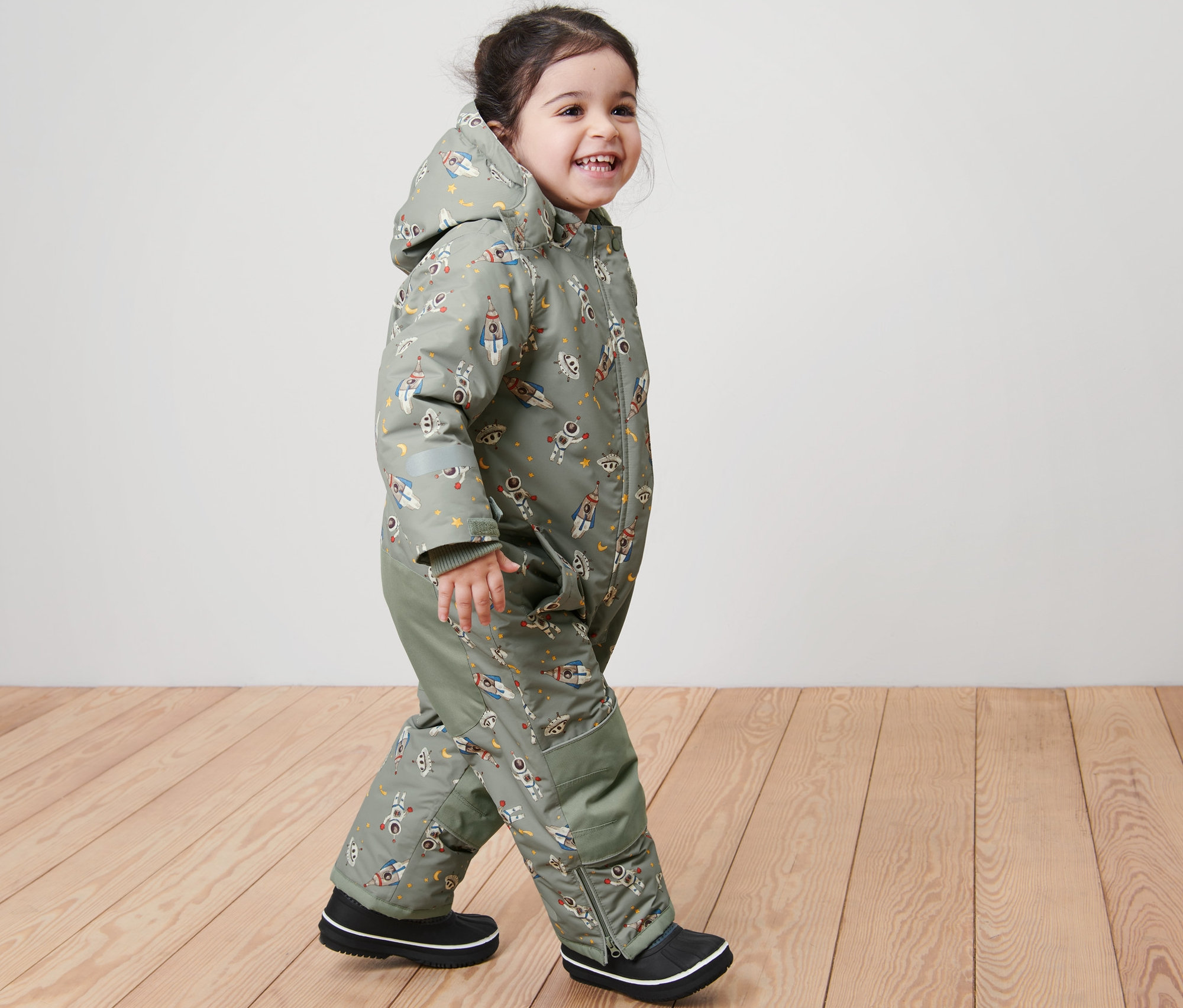 Lächelndes Kind geht und trägt einen Kinder-Schneeanzug mit Weltraumdruck.