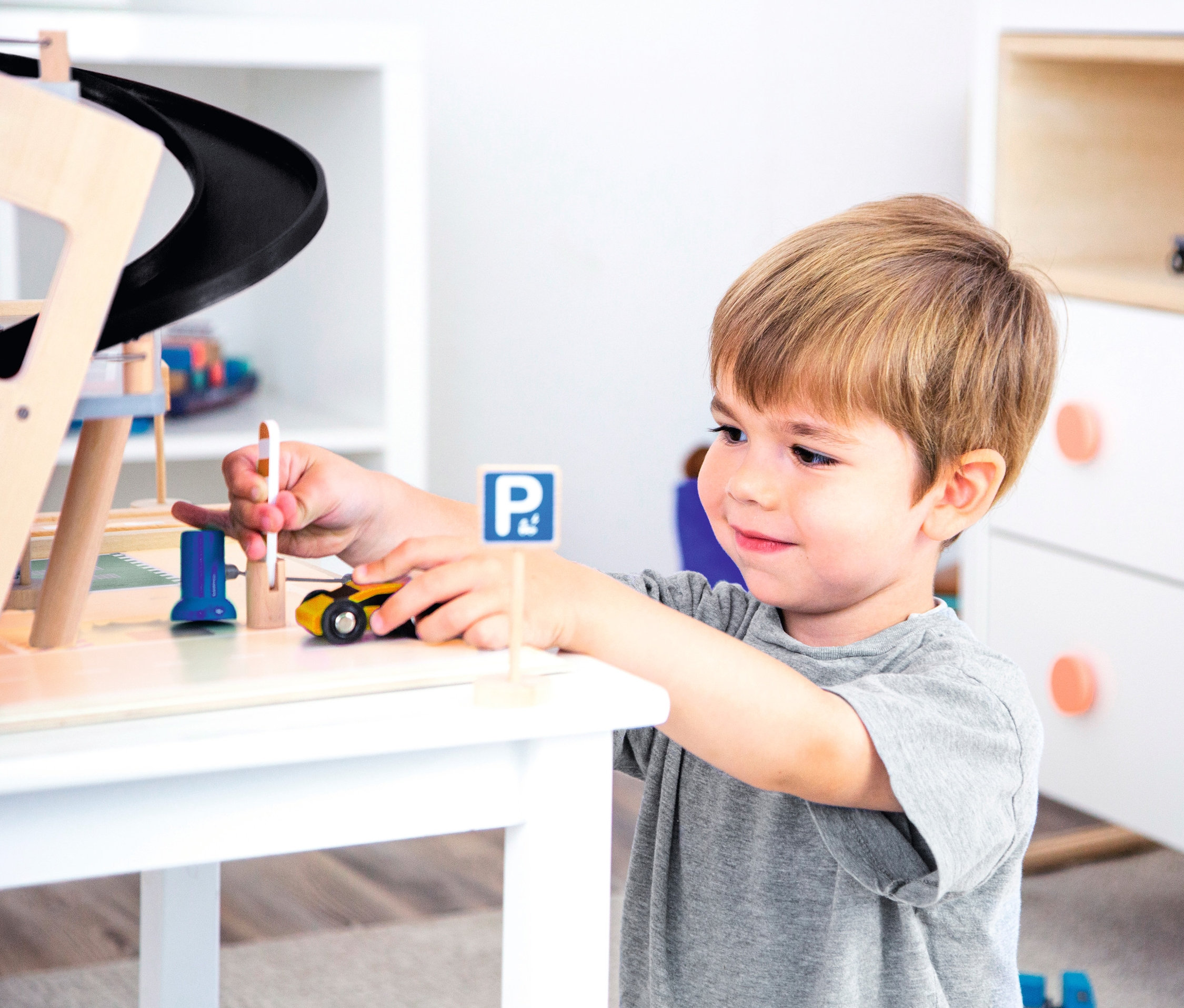 Ein Junge spielt mit einem hölzernen small foot Parkhaus »Rallye« auf einem weißen Tisch.
