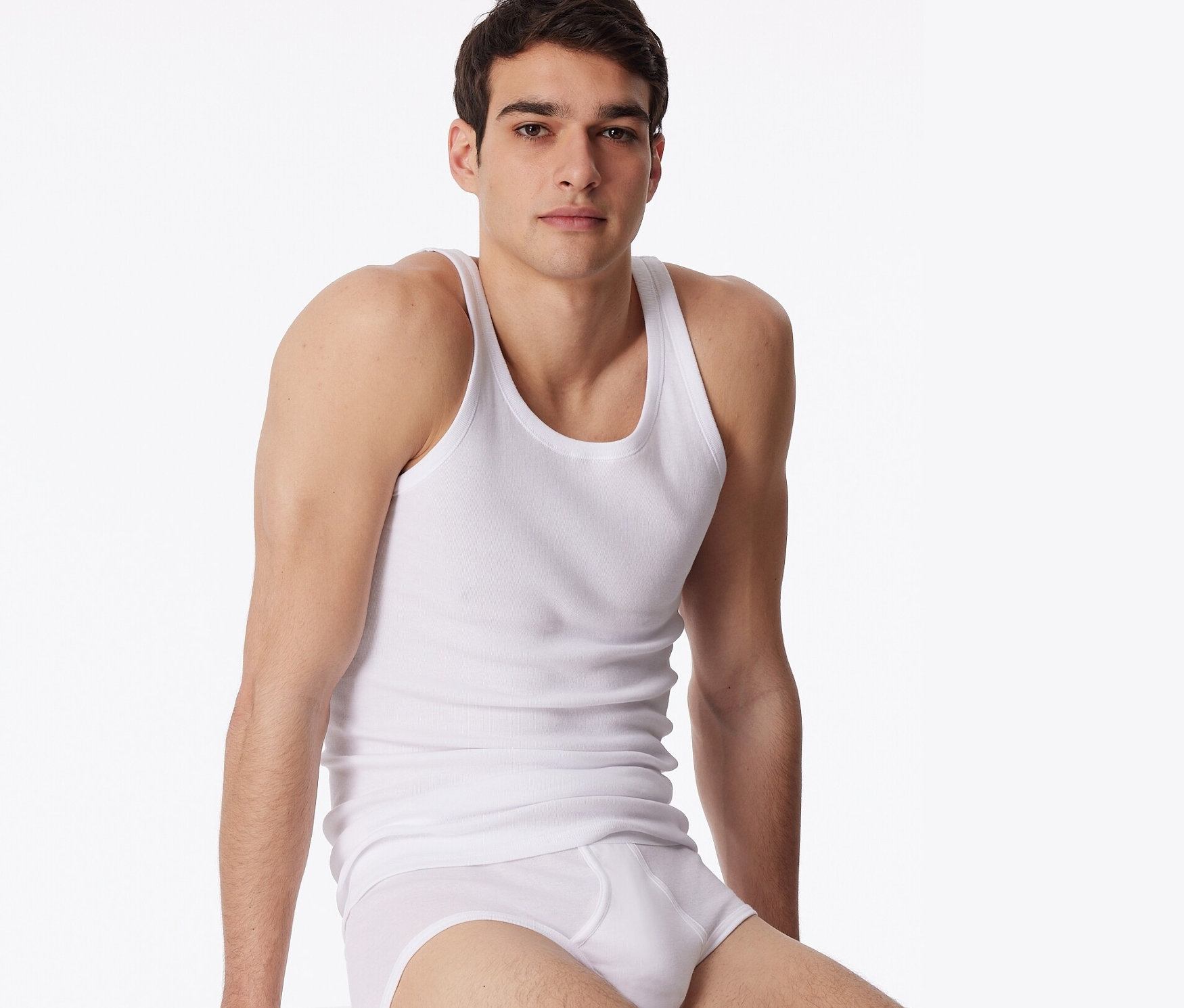 Mann sitzt auf einem weißen Würfel und trägt weiße Unterwäsche und ein weißes 2 SCHIESSER Unterhemd in Feinripp.