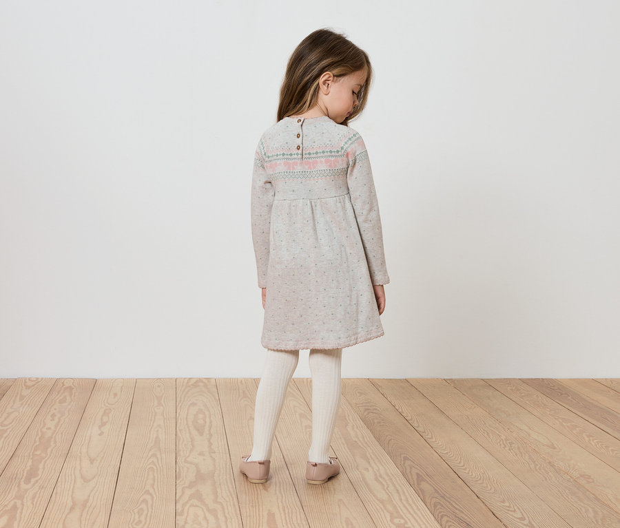 Mädchen in langärmligem Kleid steht mit dem Rücken zur Kamera.