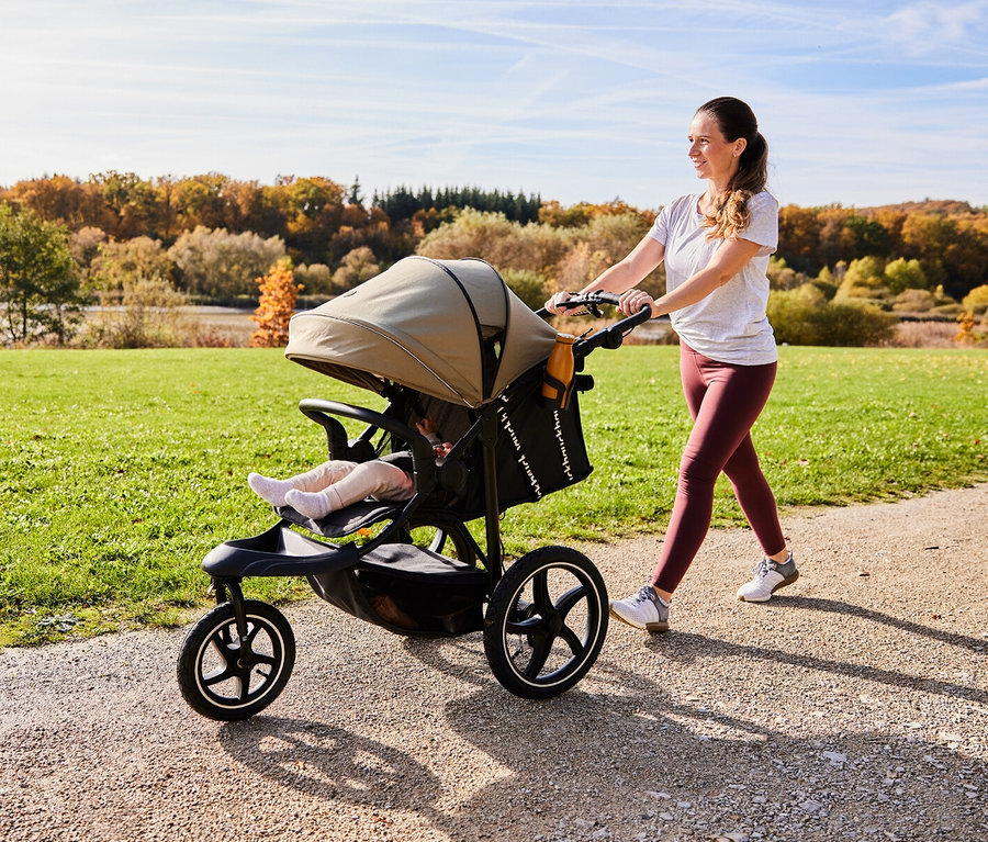Eine Frau schiebt einen Kinderwagen auf einem Feldweg entlang.
