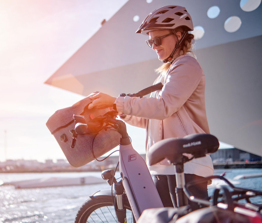 Frau mit Helm befestigt eine FISCHER Lenkertasche PLUS Cita an einem E-Bike.