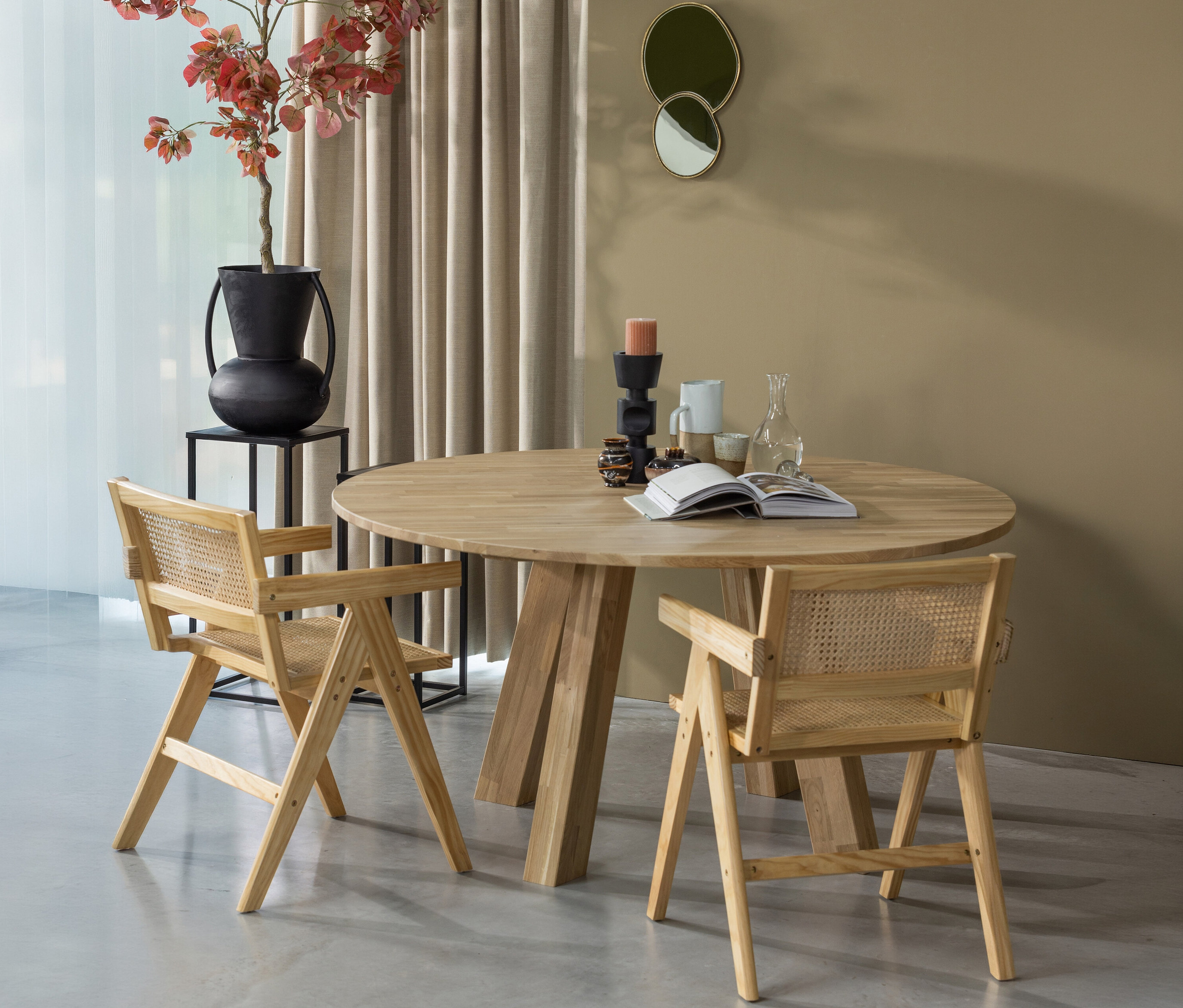 Zwei Holzstühle stehen am runden WOOOD »Rhonda« Esstisch (ca. 150 cm). Auf dem Tisch liegen ein Buch, Kerzen und Gläser.