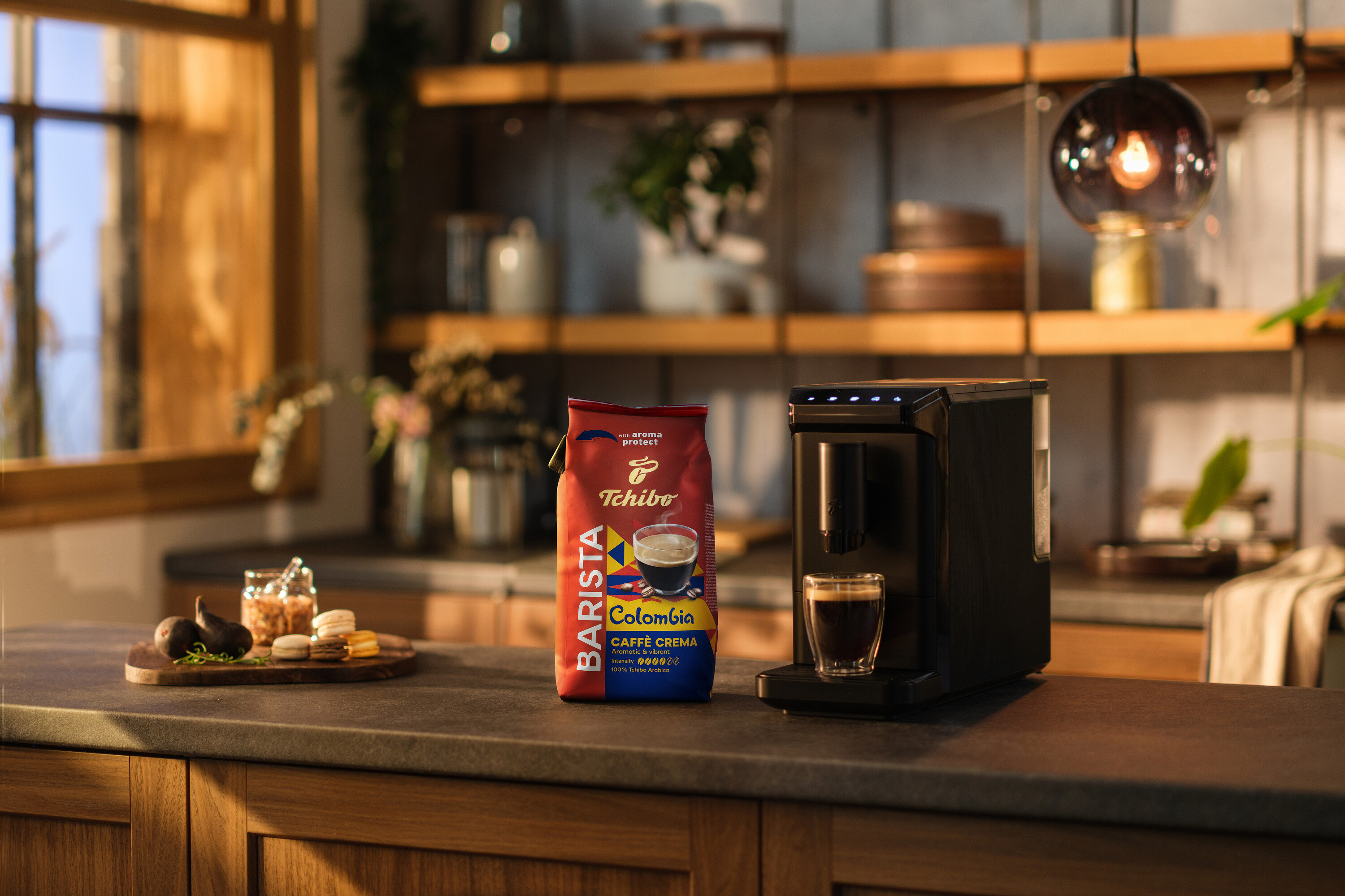 Auf einer Küchentheke stehen eine Kaffeemaschine, eine Tasse Kaffee und eine Packung BARISTA Origins Colombia - 1 kg Ganze Bohne.