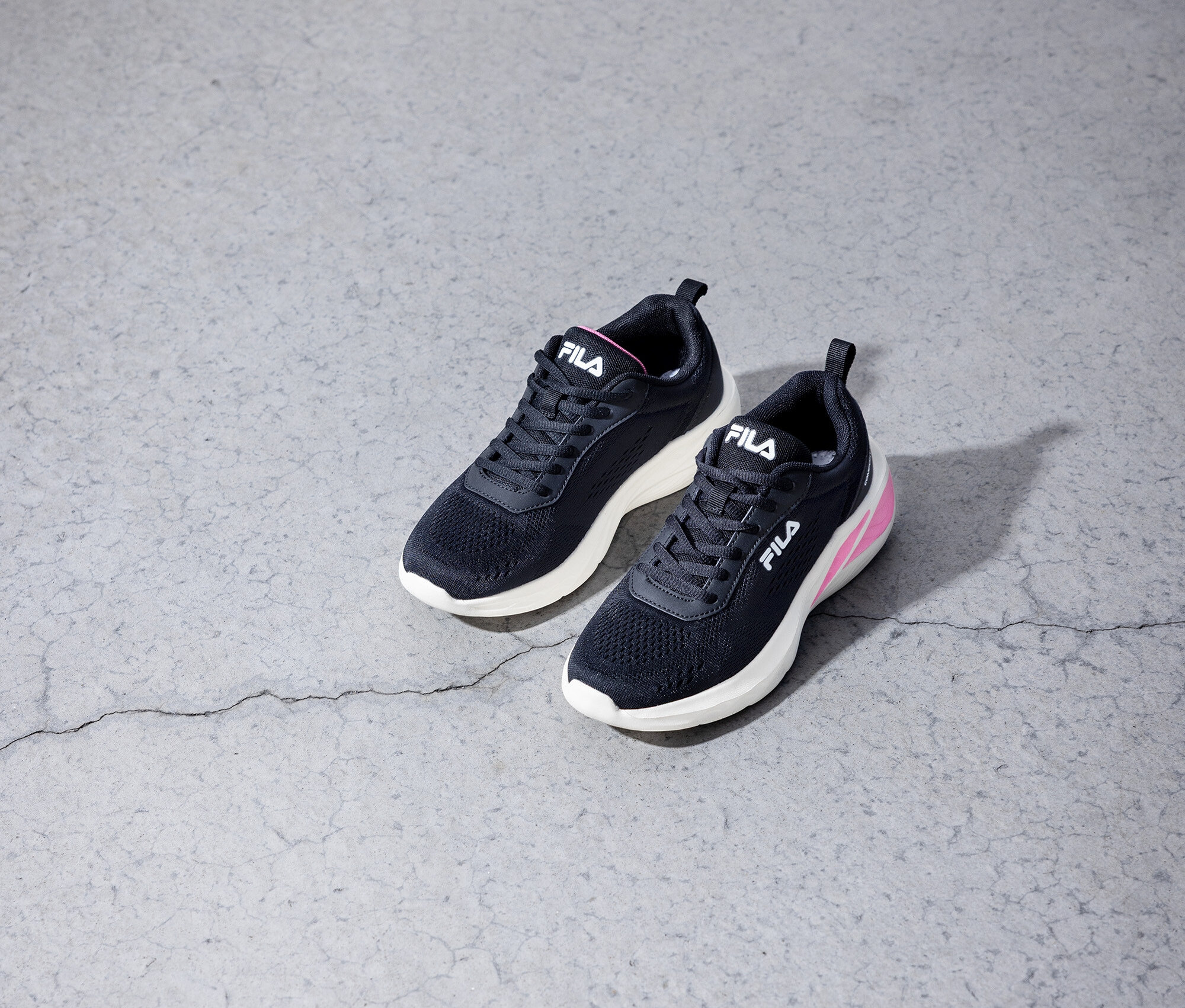 Zwei schwarze Fila-Sneakers stehen auf einem grauen Betonboden.