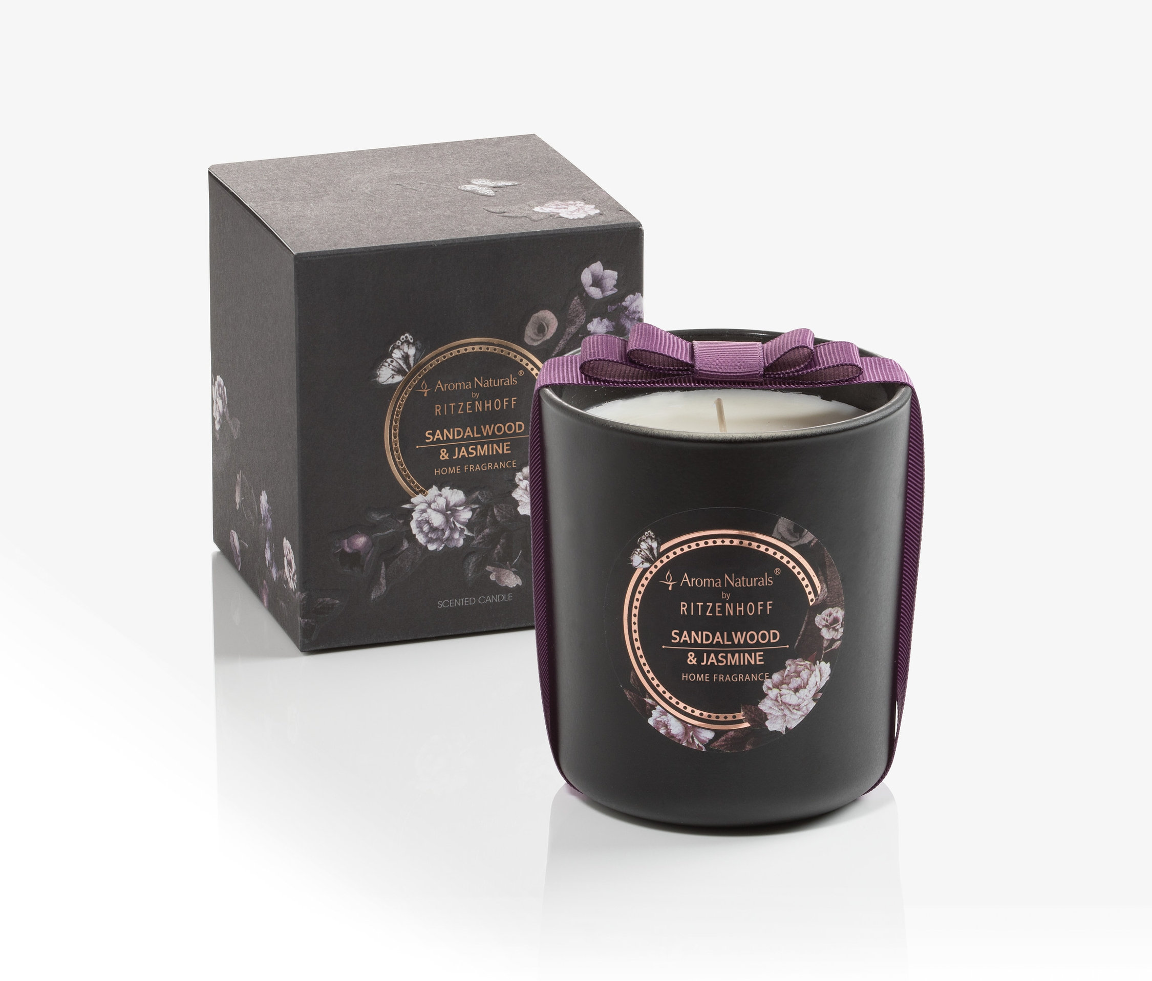 Eine schwarze Kerze mit lila Schleife neben einer schwarzen Schachtel auf weißem Hintergrund.