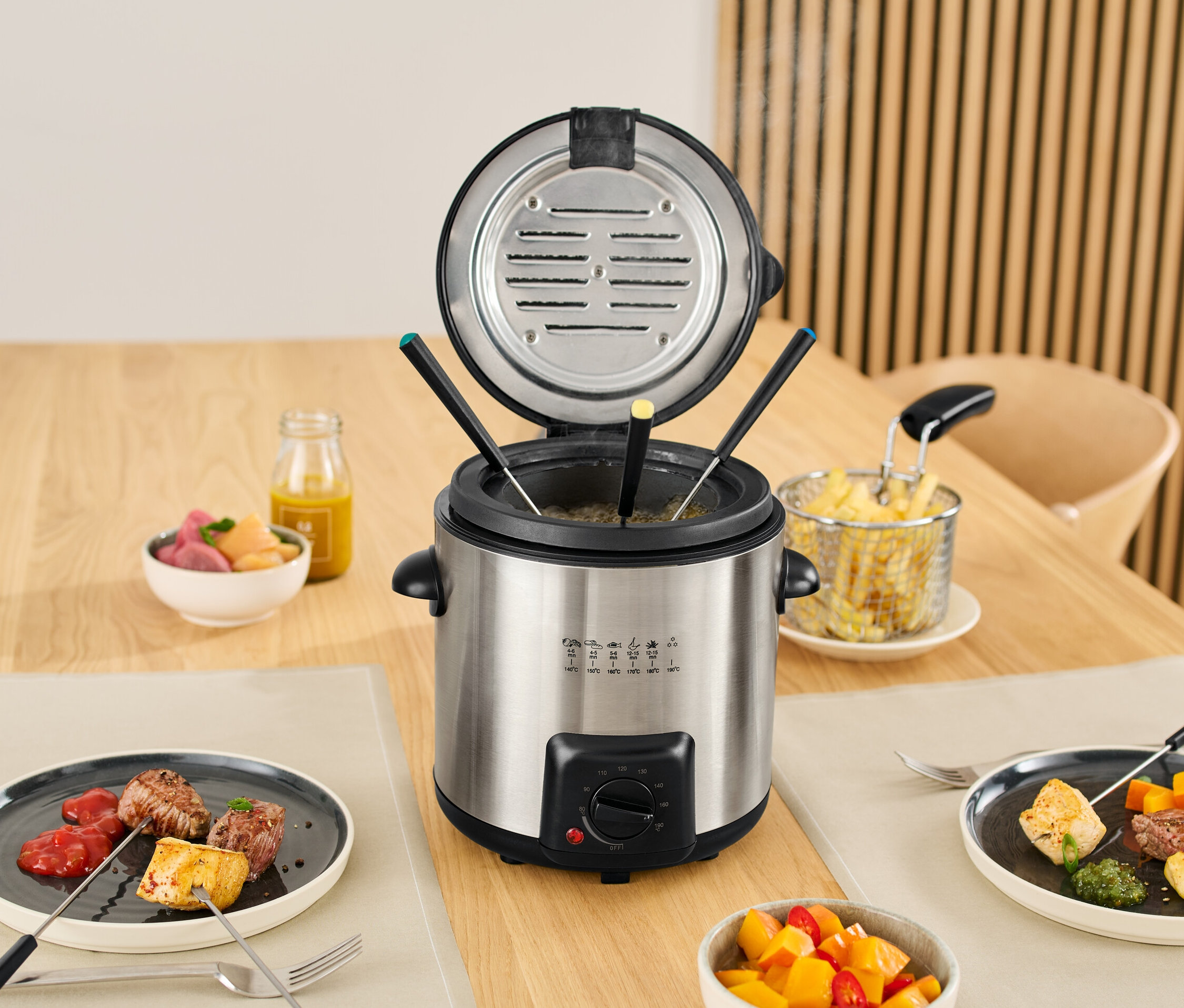 Mini-Fritteuse-und-Fondue steht auf einem Tisch mit Speisen auf Tellern und in Schüsseln.