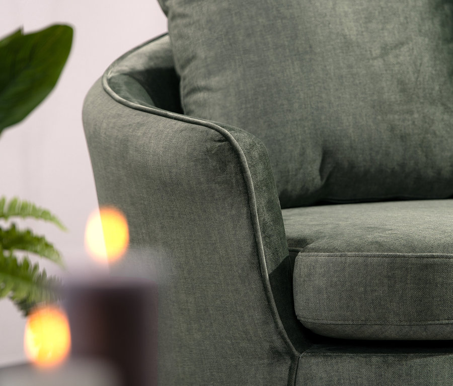 Nahaufnahme des Sessels »Miranda«, dunkelgrün, teilweise verdeckt durch Pflanze und Kerzen.
