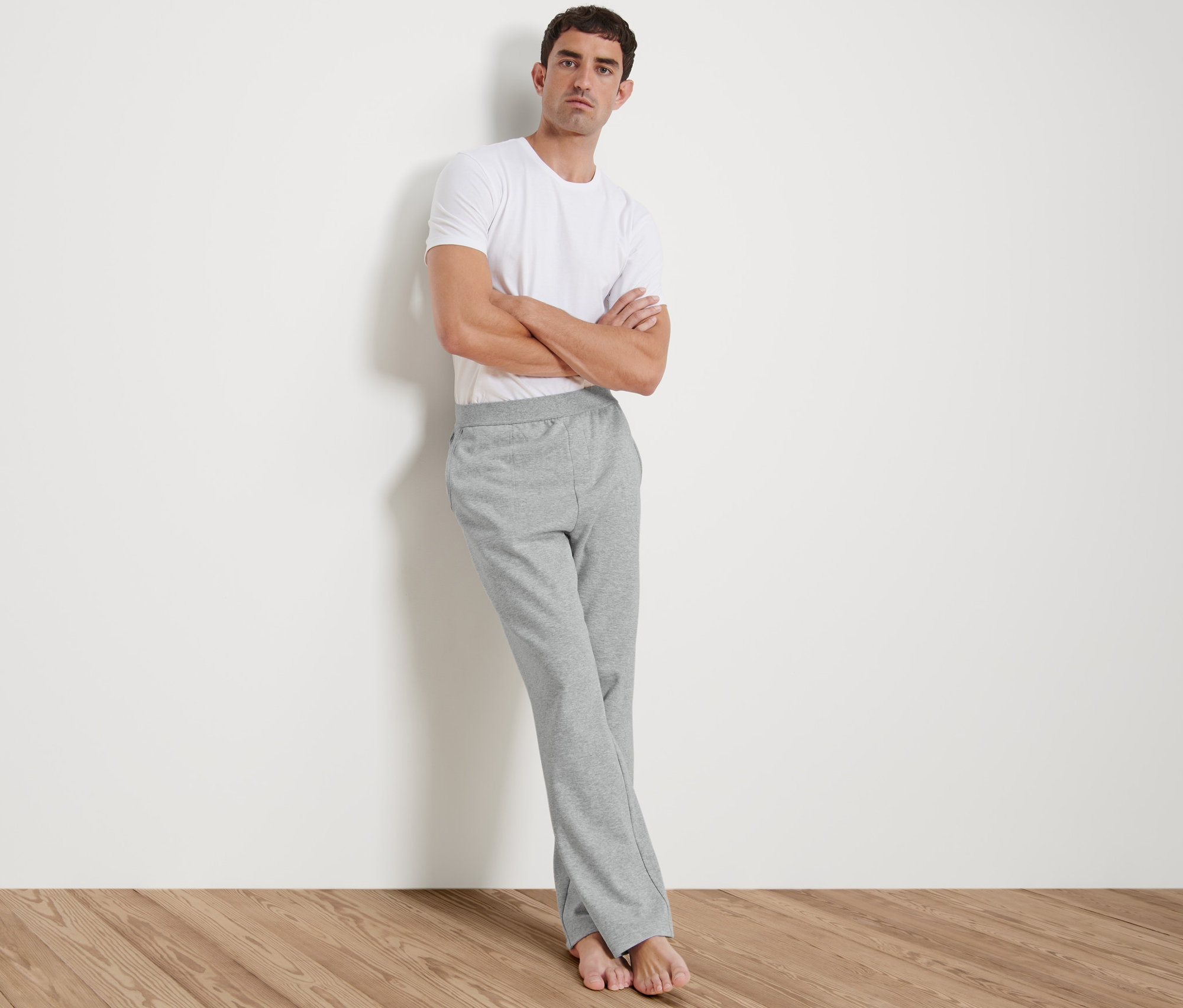 Mann lehnt an Wand, trägt weißes T-Shirt und Homewearhose.