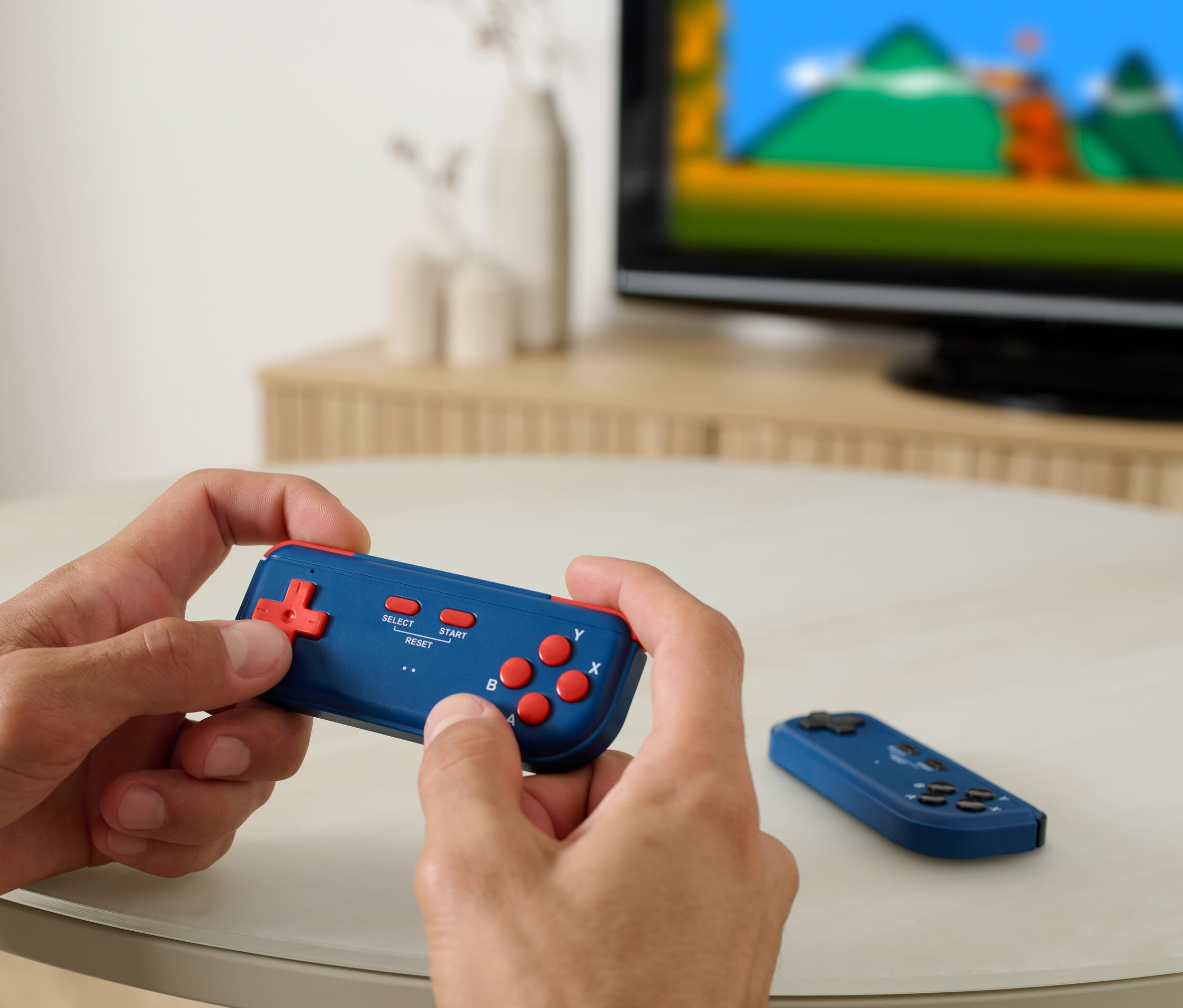 Mann spielt Retro-TV-Spielekonsole, im Hintergrund ist ein Fernseher zu sehen.