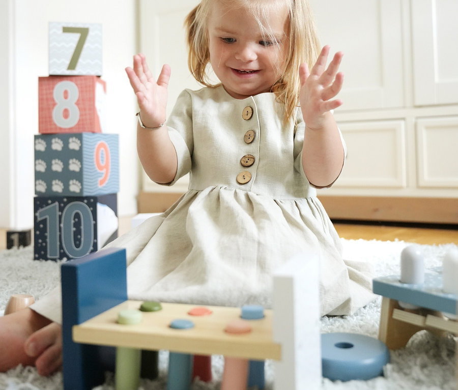 Mädchen sitzt auf Teppich und spielt mit Holzspielzeug und Zahlenwürfeln. Zu sehen ist ein small foot Motorikspiele-Set »Arctic«.
