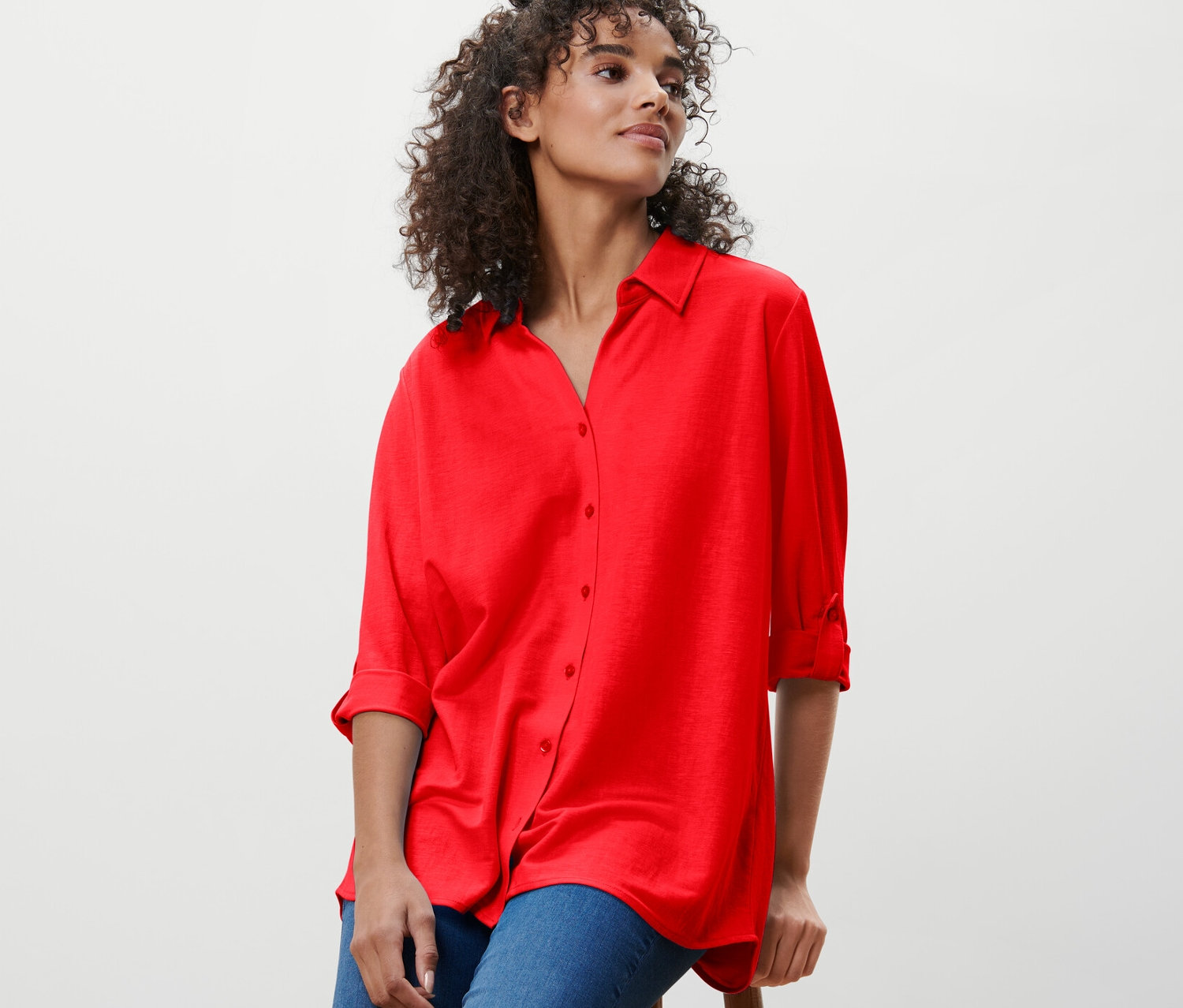 Frau sitzt auf einem Hocker und trägt eine rote Piqué-Jerseybluse.