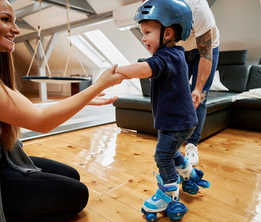 Frau hält Hände von kleinem Jungen mit Helm und in zyanfarbenen HUDORA My First Quad Rollschuhen.
