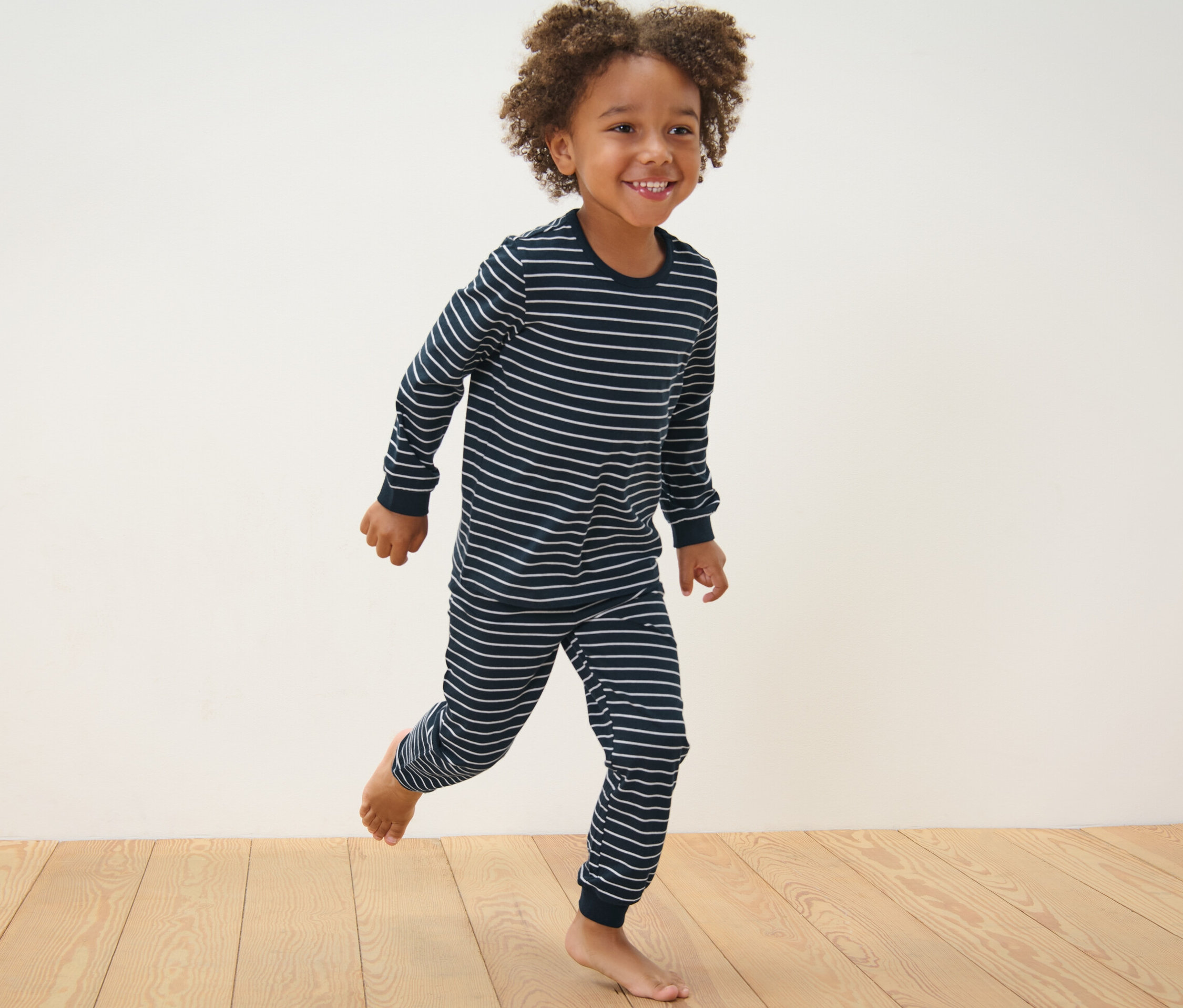 Ein Junge in einem blau gestreiften Pyjama rennt auf einem Holzboden. 2 Kinder-Pyjamas, blau.