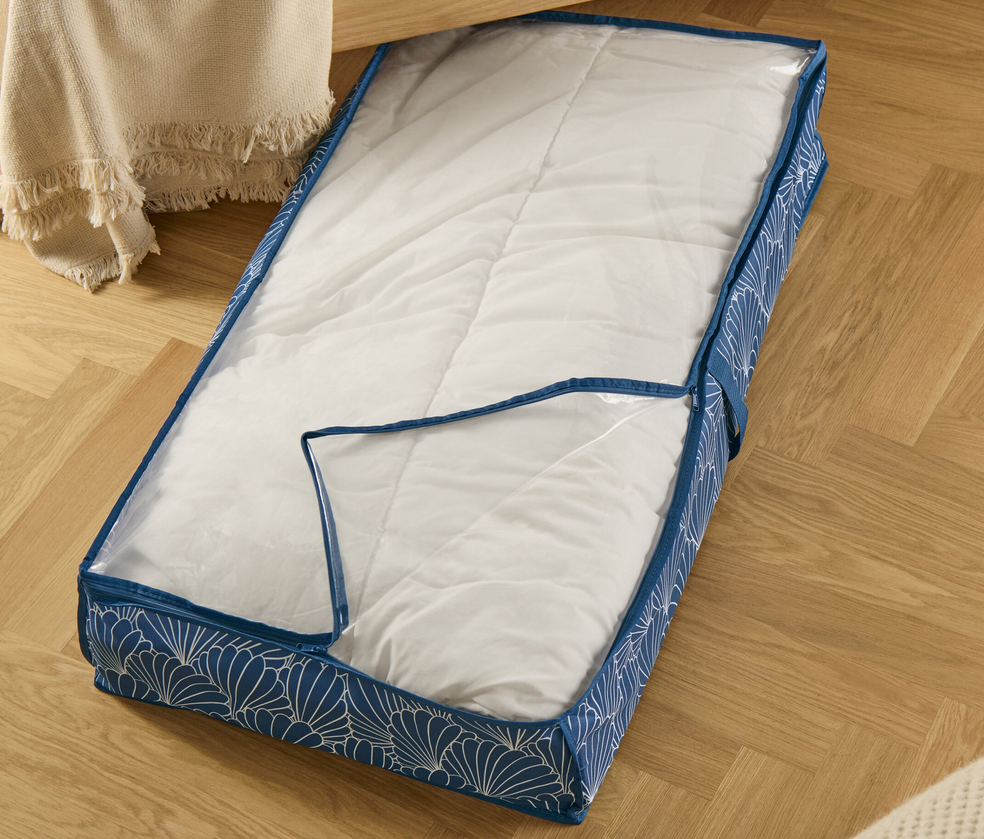 Blauer Unterbettkommode mit weißem Muschelmuster, teilweise transparent, liegt auf Parkettboden.