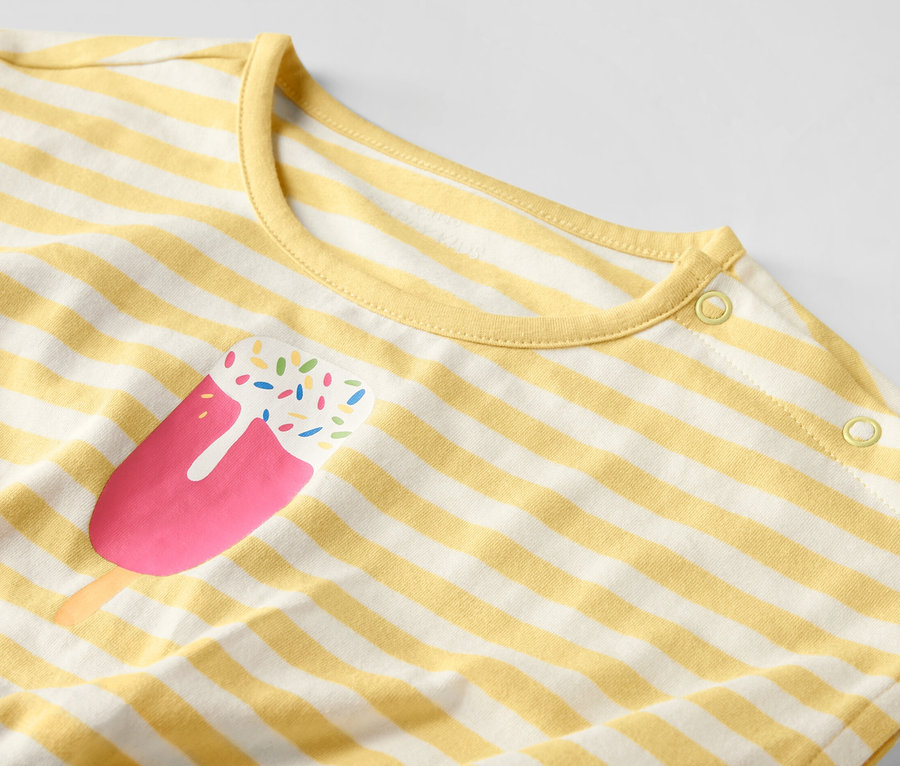 Detailansicht eines Kinder-Jumpsuits mit gelben und weißen Streifen und Eis am Stiel-Aufdruck.