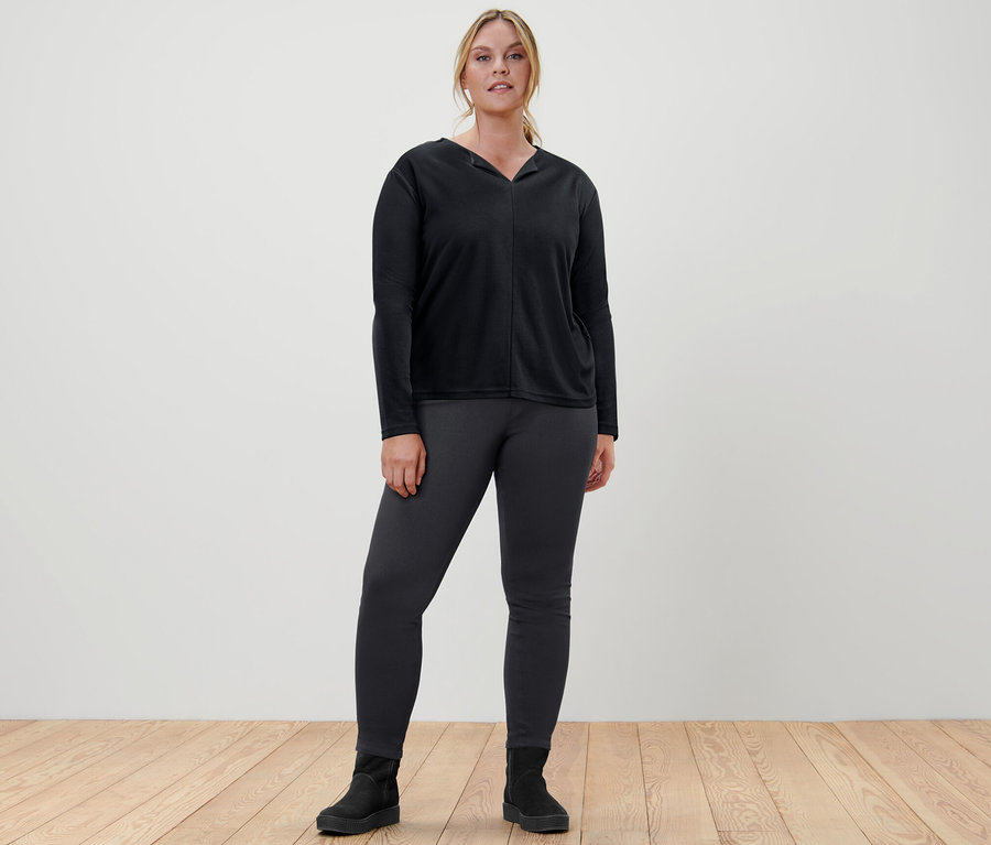 Frau steht in schwarzem Blusenshirt und Jeggings.